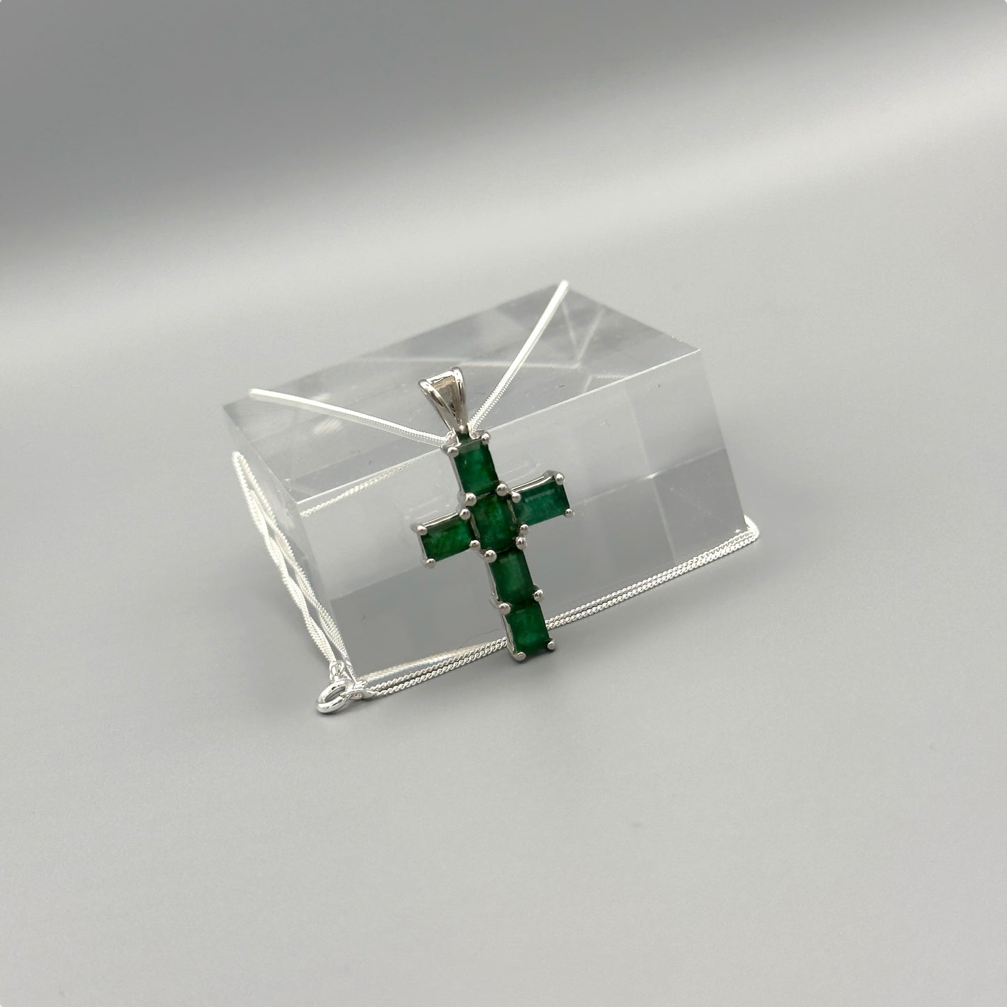 Emerald cross pendant on silver box chain displayed on clear block