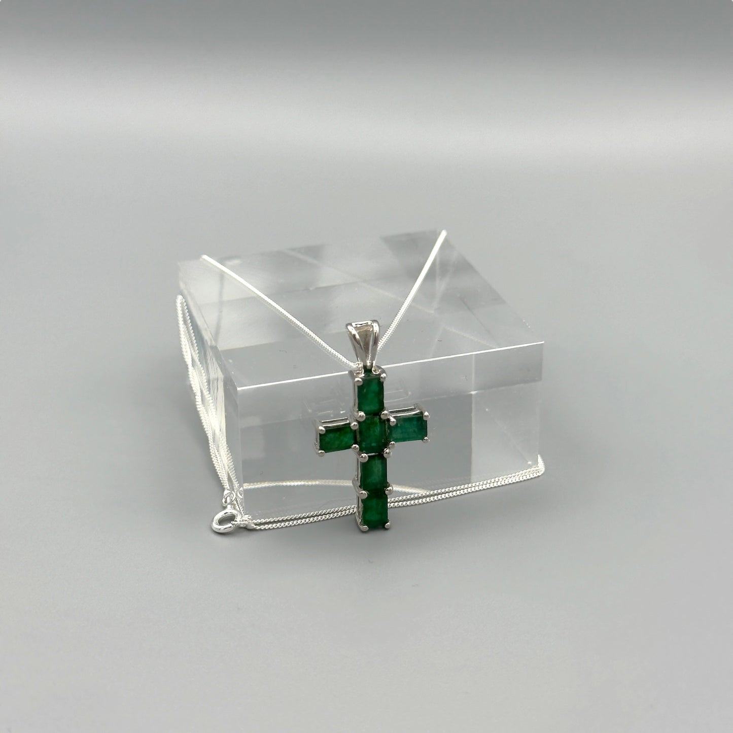 Front-facing view of emerald cross necklace with bright silver detail