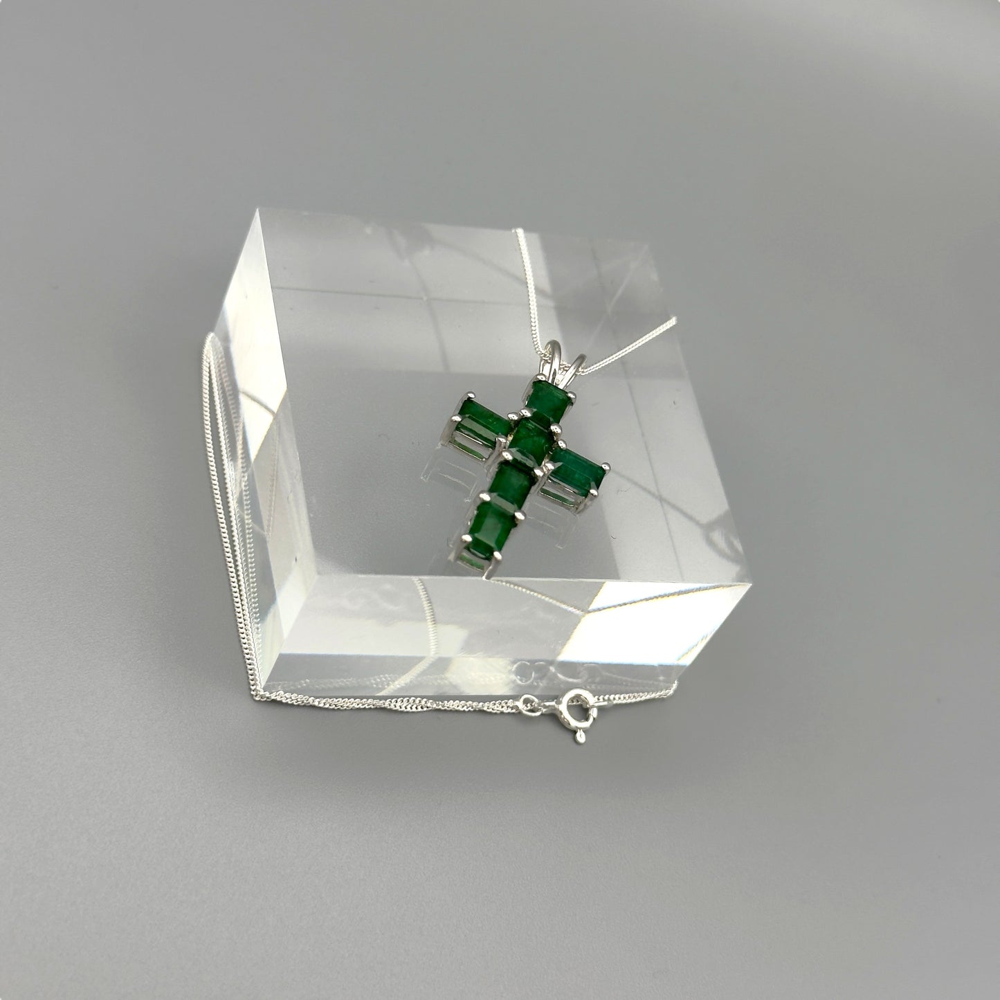 Angled emerald cross necklace on display block with reflections