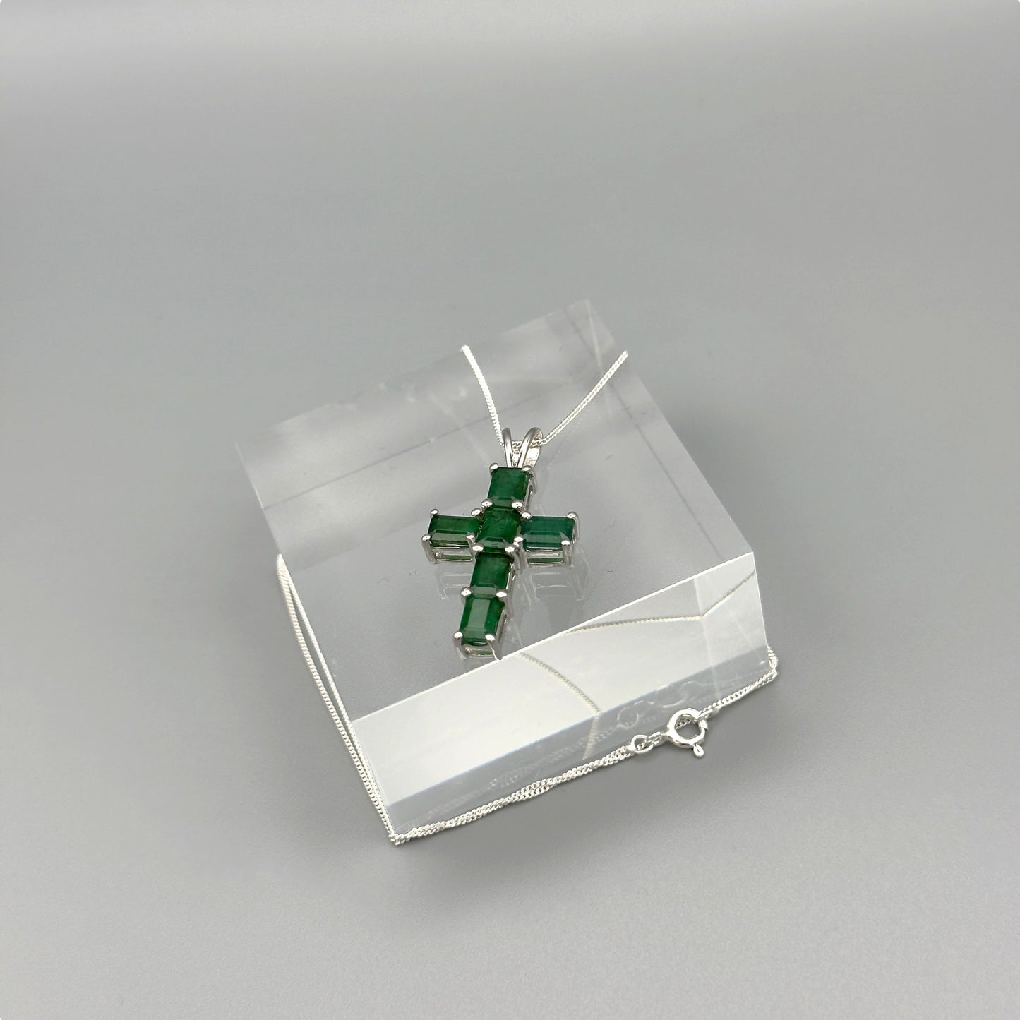 Full view of silver cross necklace laid over crystal block