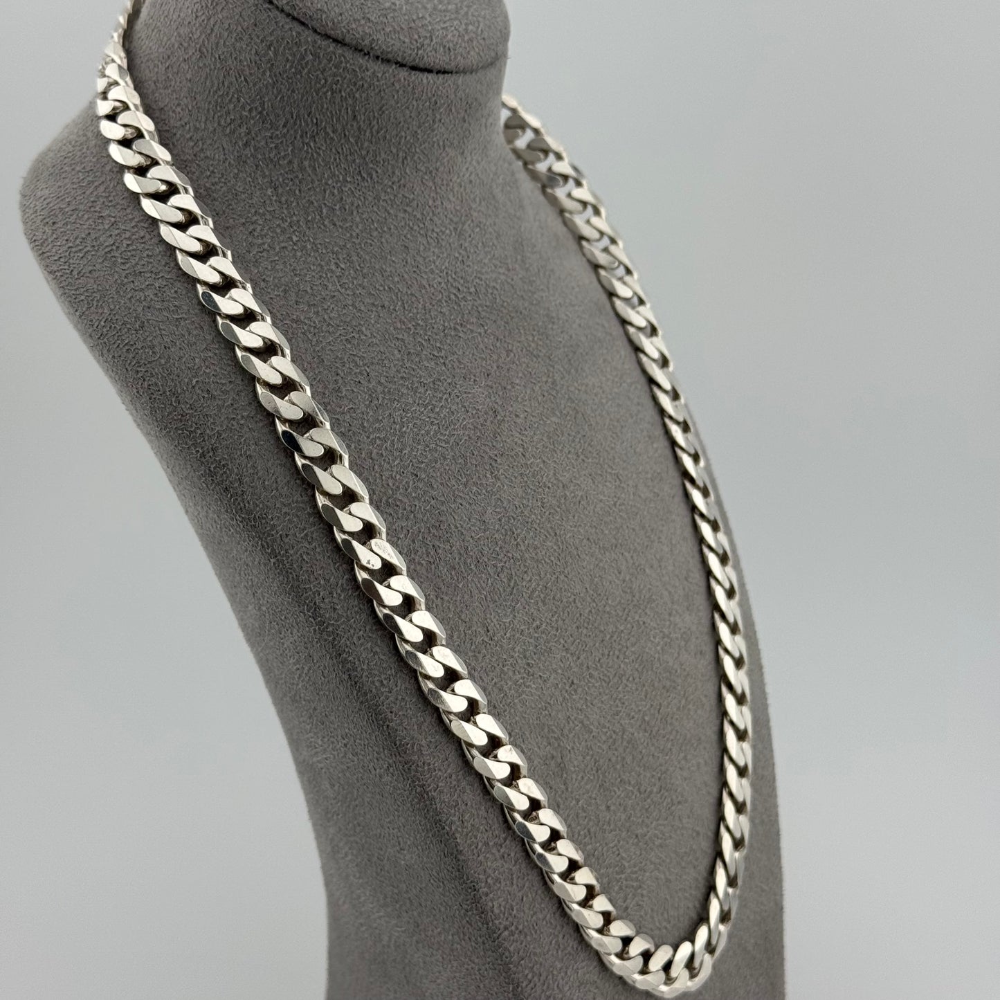 Silver chain necklace on a mannequin bust against a gray background