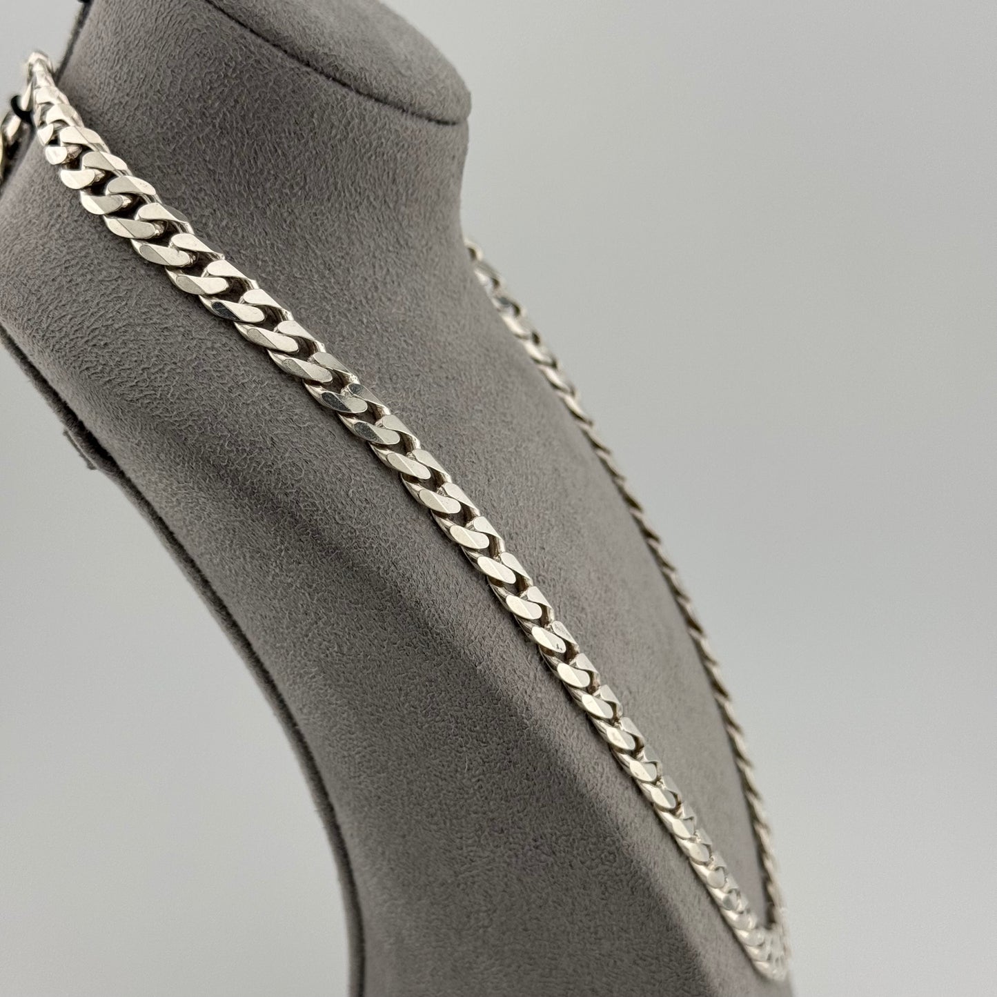 Silver chain necklace on a mannequin bust against a gray background