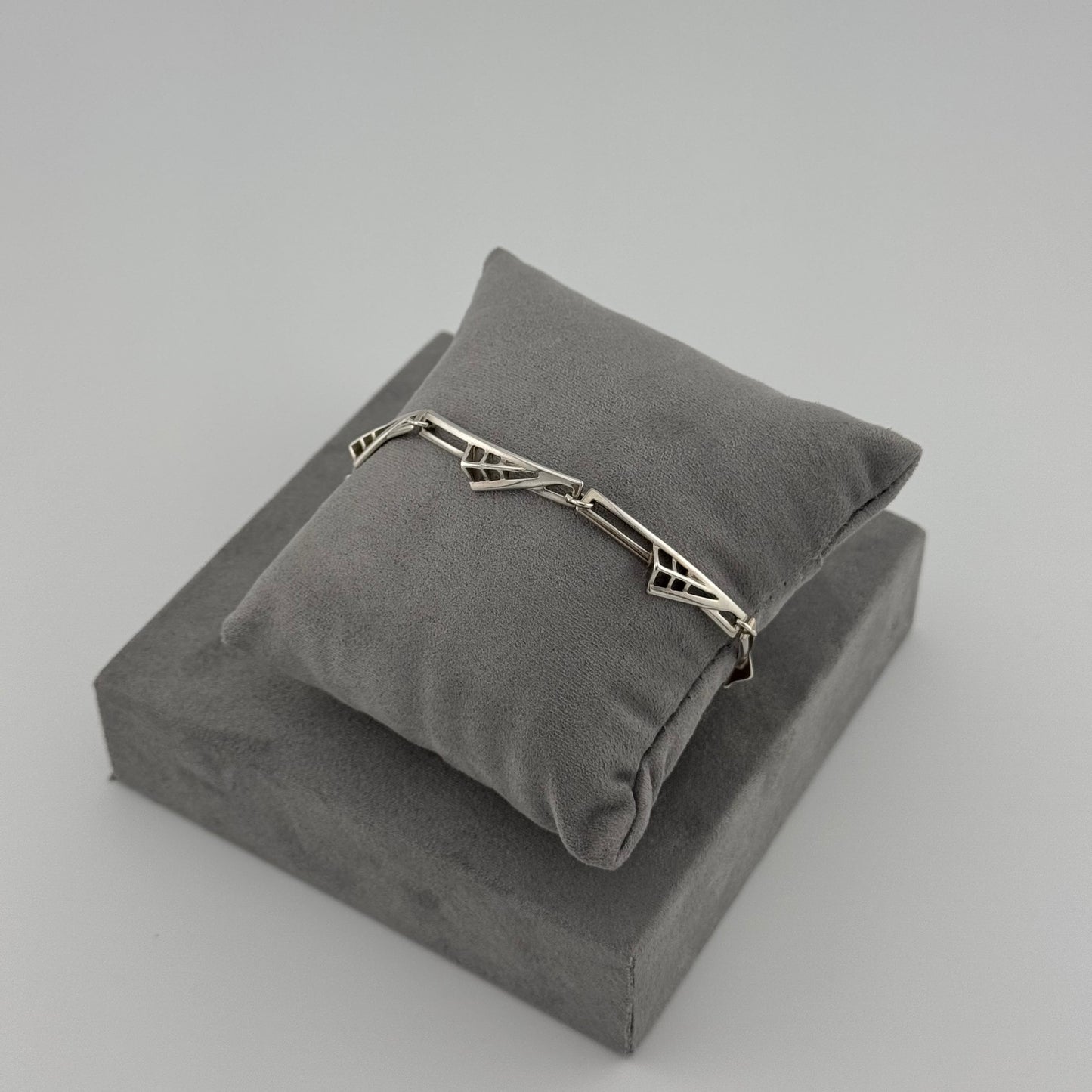 silver bracelet with a geometric pattern n a grey cushion