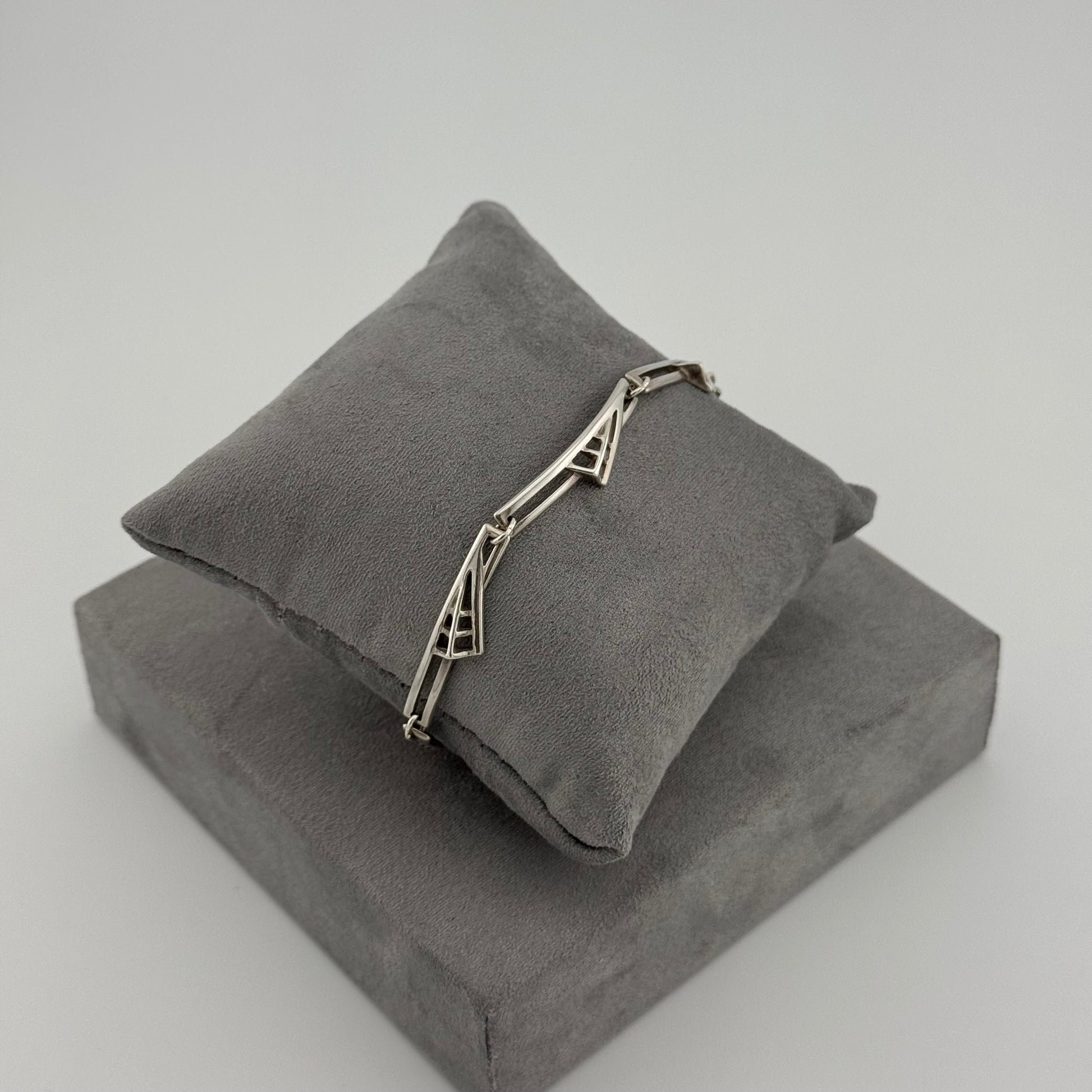 silver bracelet with a geometric pattern n a grey cushion
