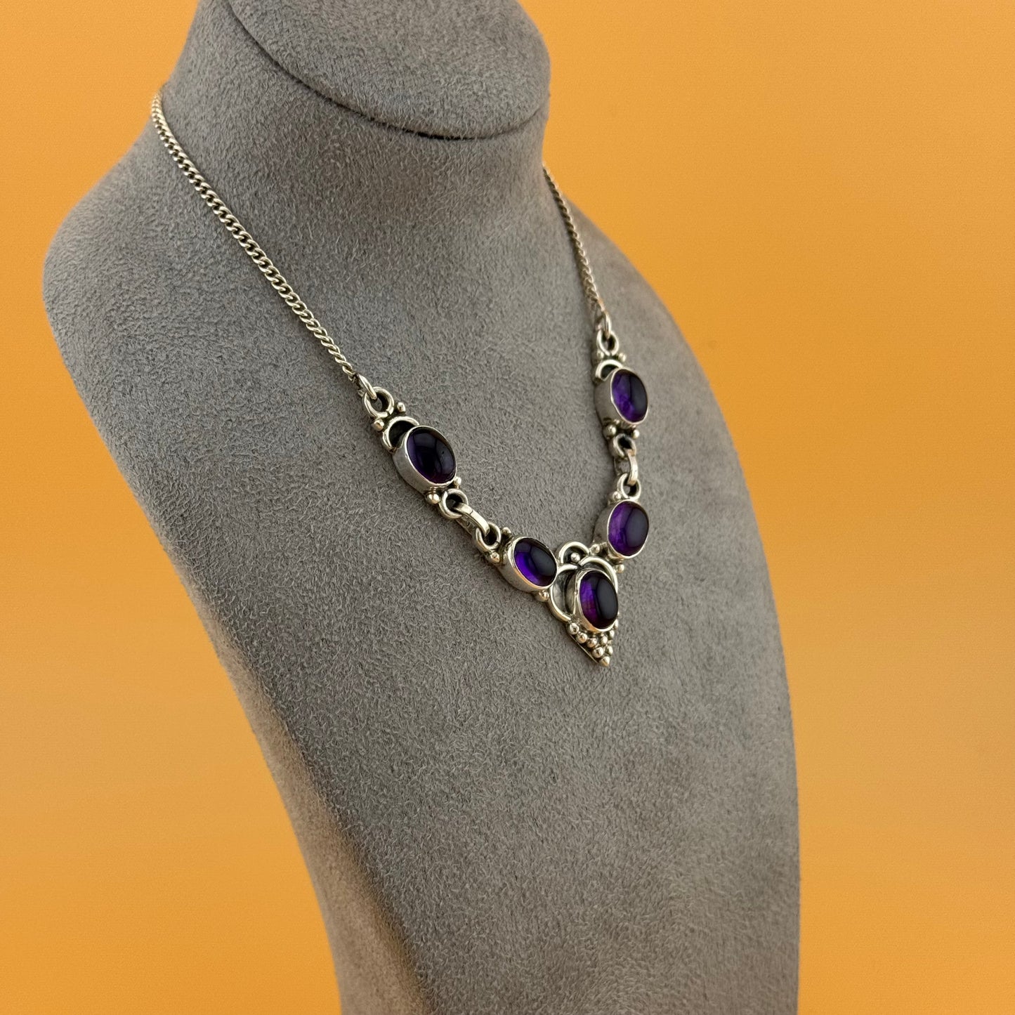 Necklace with purple amethyst stones on a gray mannequin bust against an orange background
