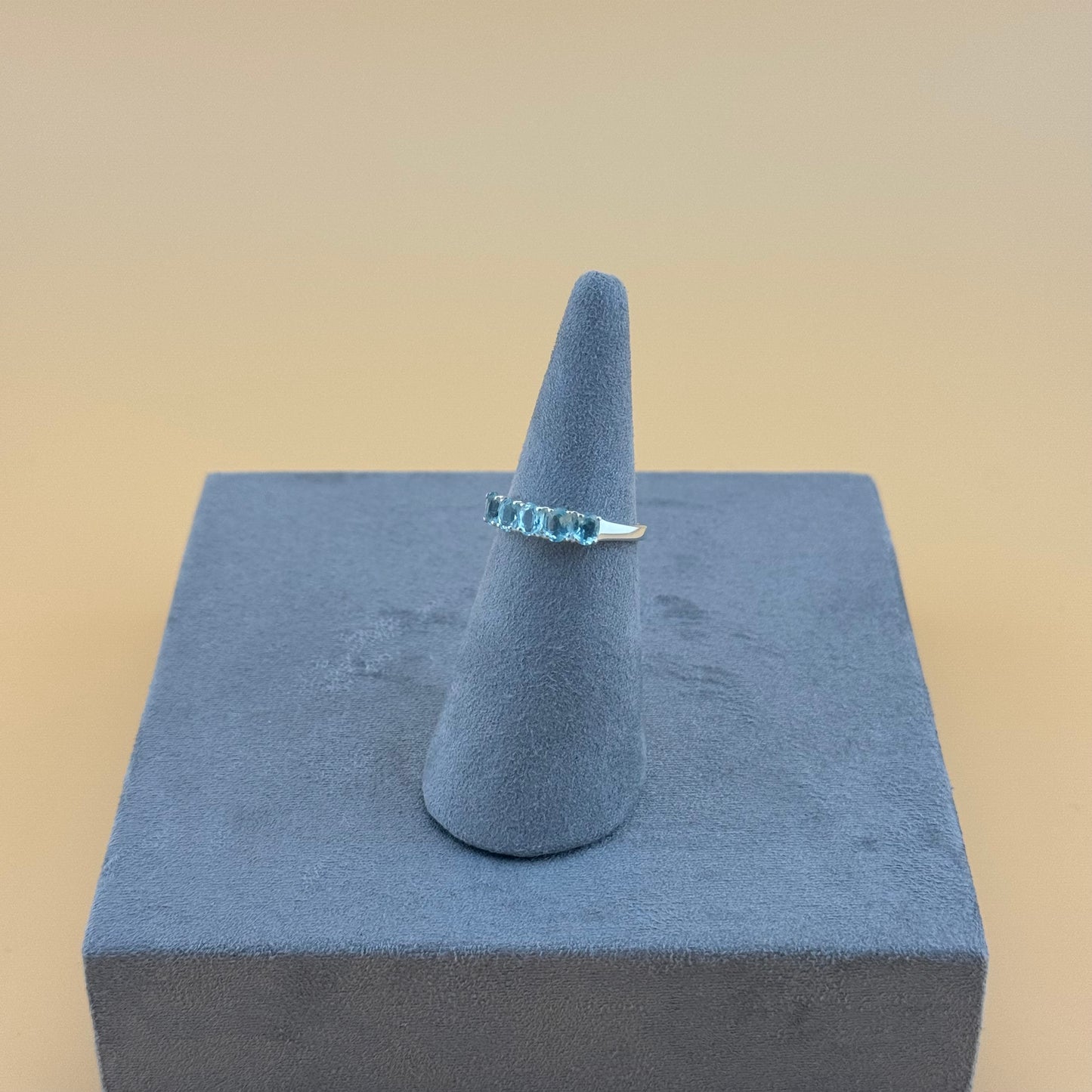 Ring with aquamarine blue gemstones on a gray cone and cube against a beige background