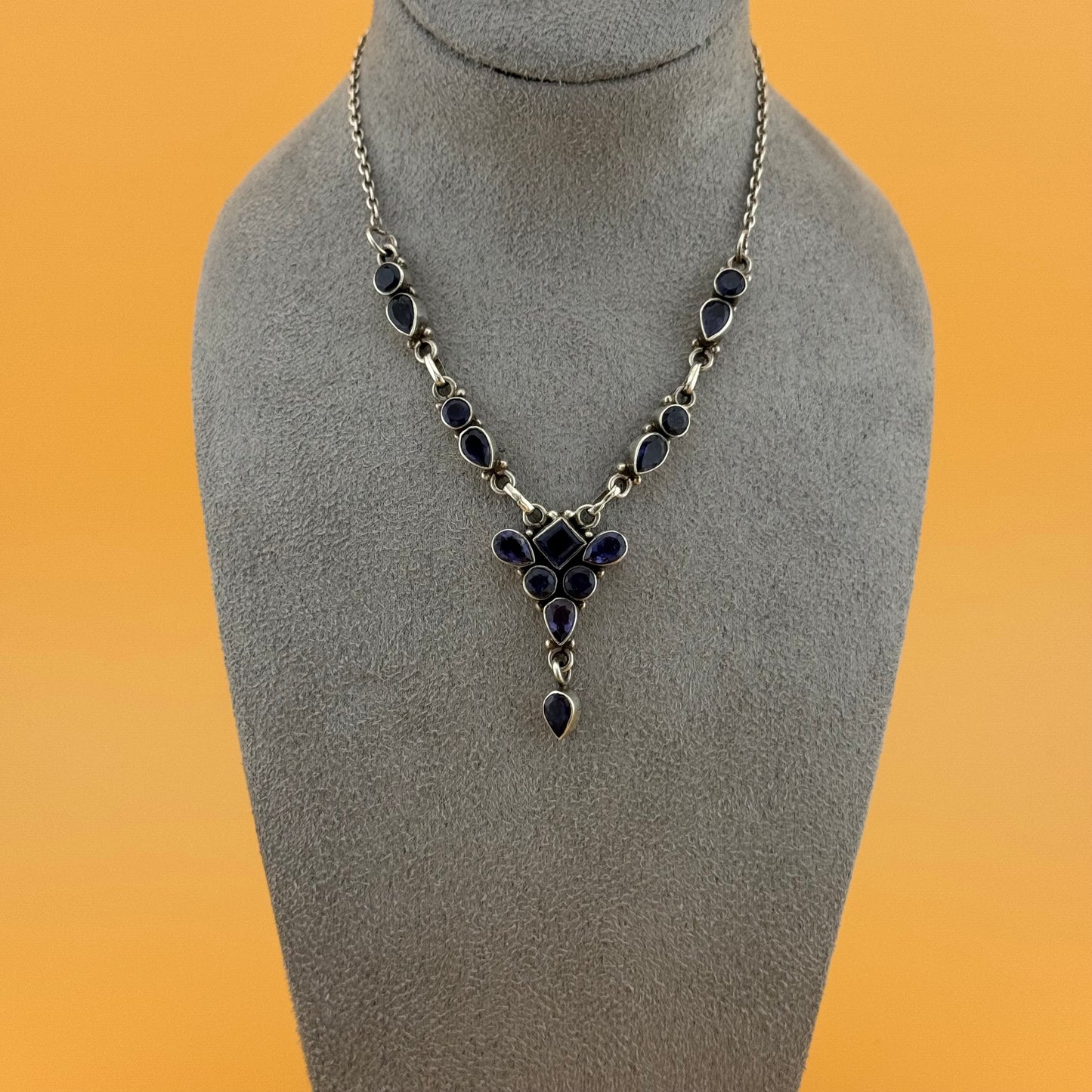 Necklace with purple iolite stones on a gray mannequin bust against an orange background
