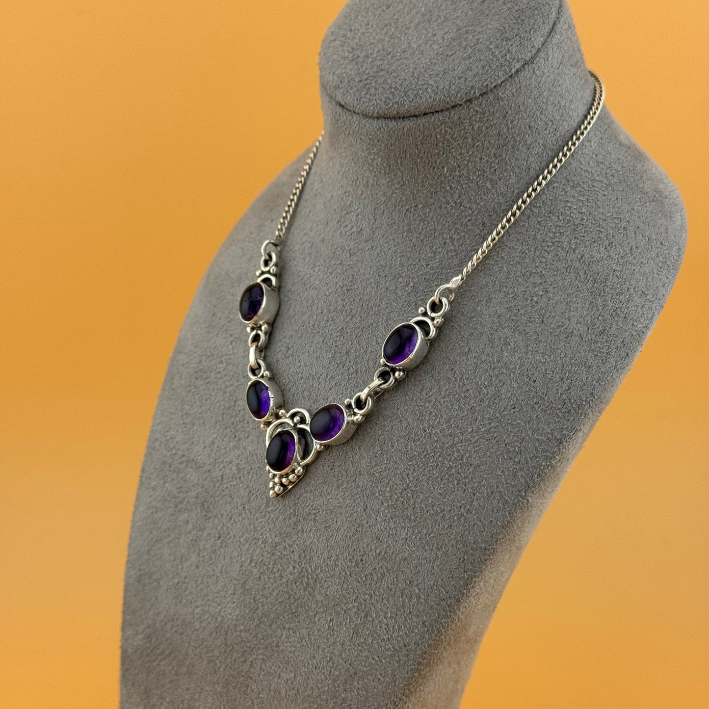 Necklace with purple amethyst stones on a gray mannequin bust against an orange background
