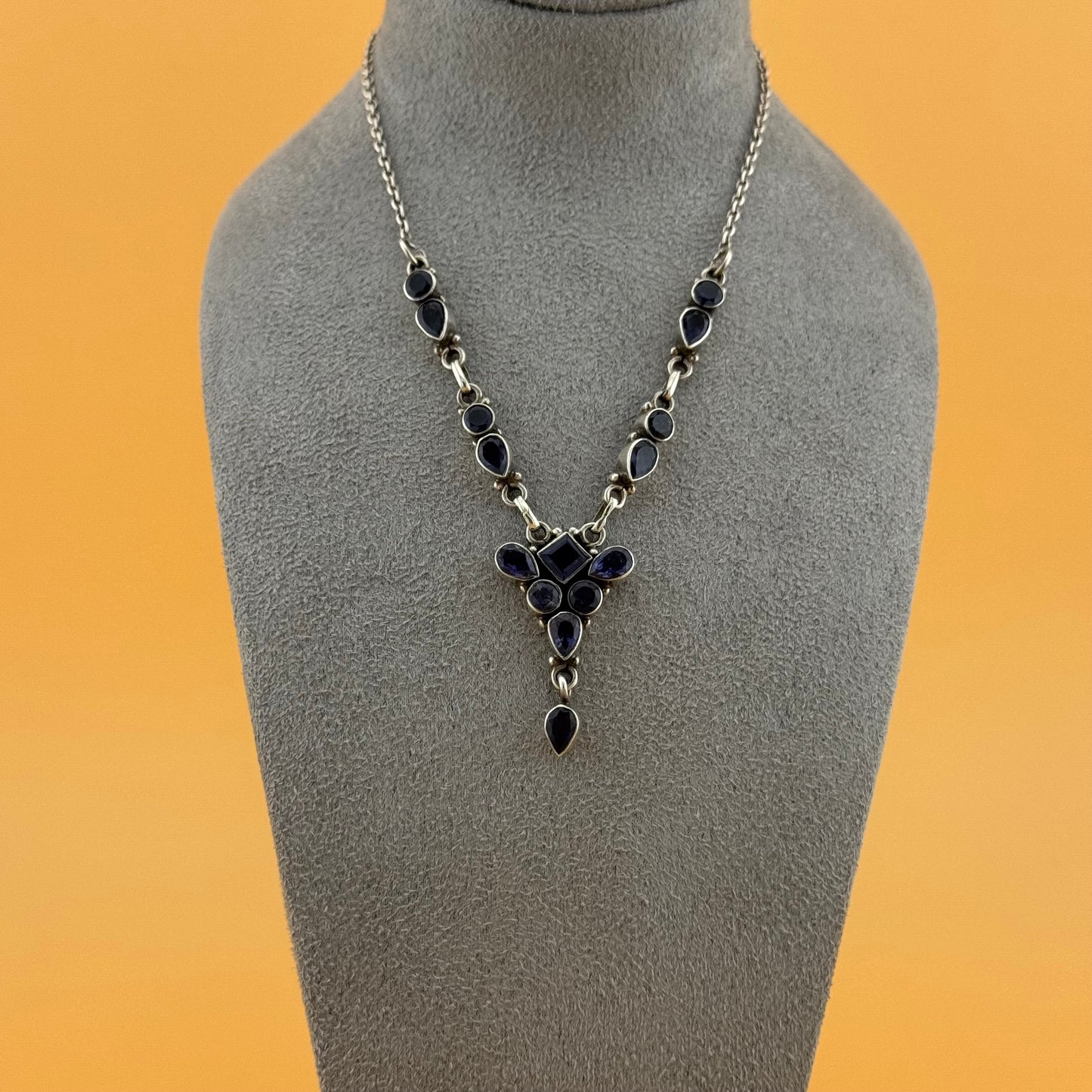 Necklace with purple stones on a gray mannequin bust against an orange background