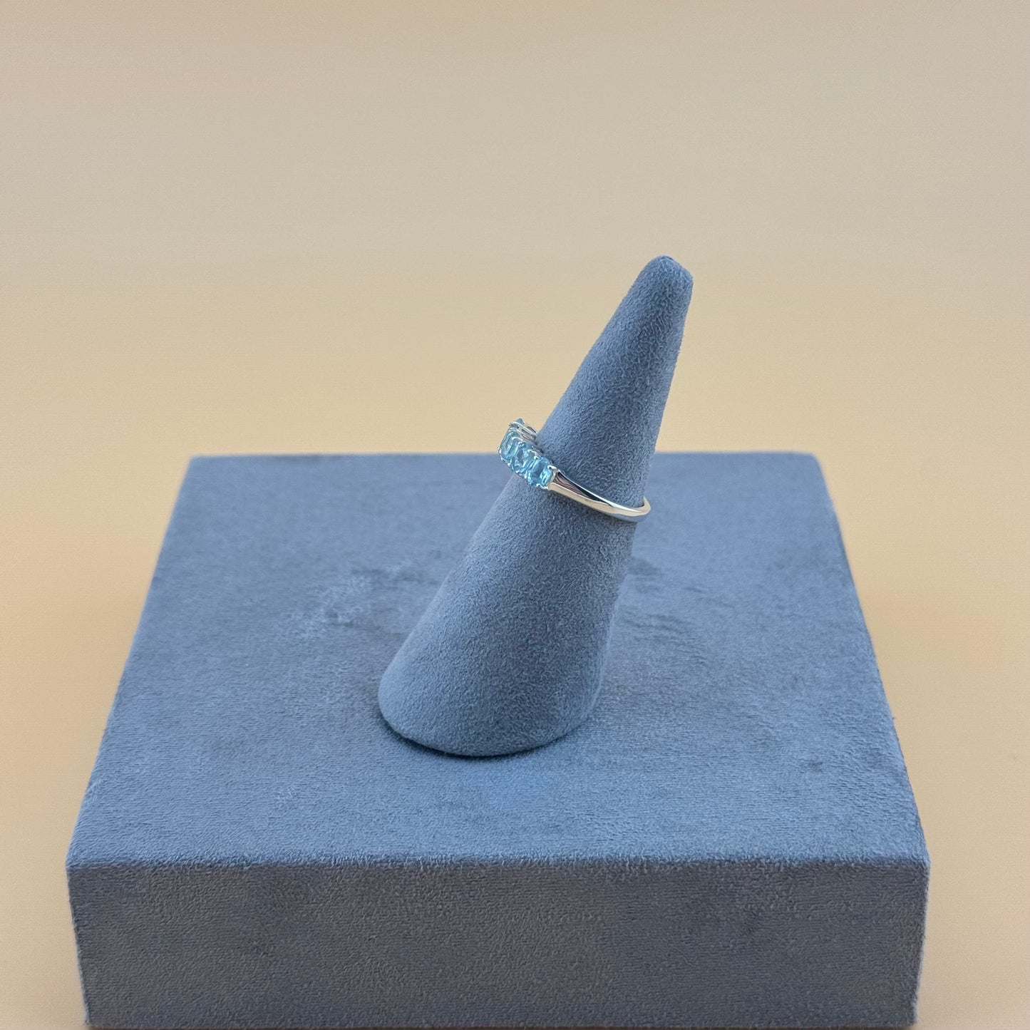 aquamarine Ring with blue gemstone on a gray stand against a beige background