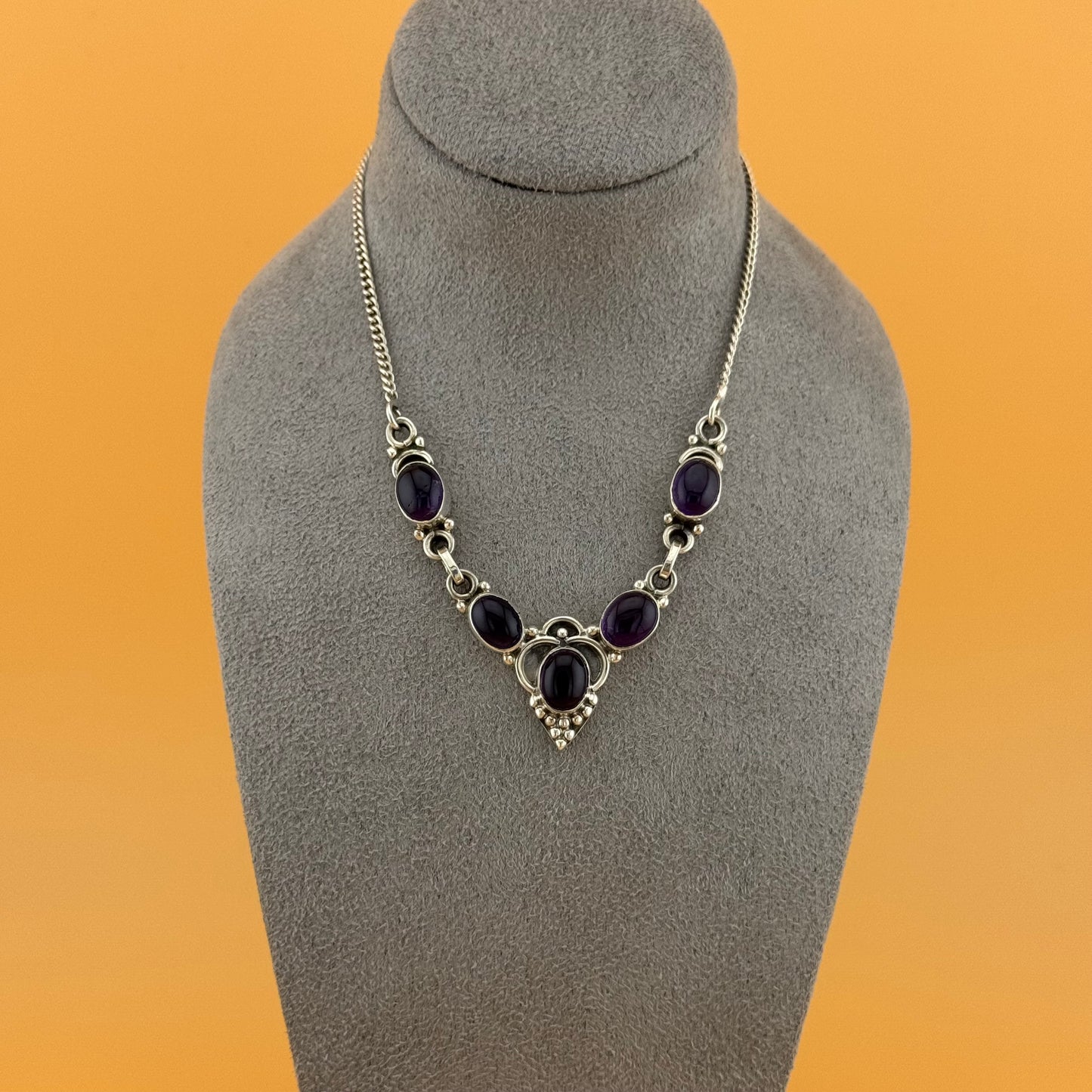 Necklace with purple amethyst stones on a gray mannequin bust against an orange background