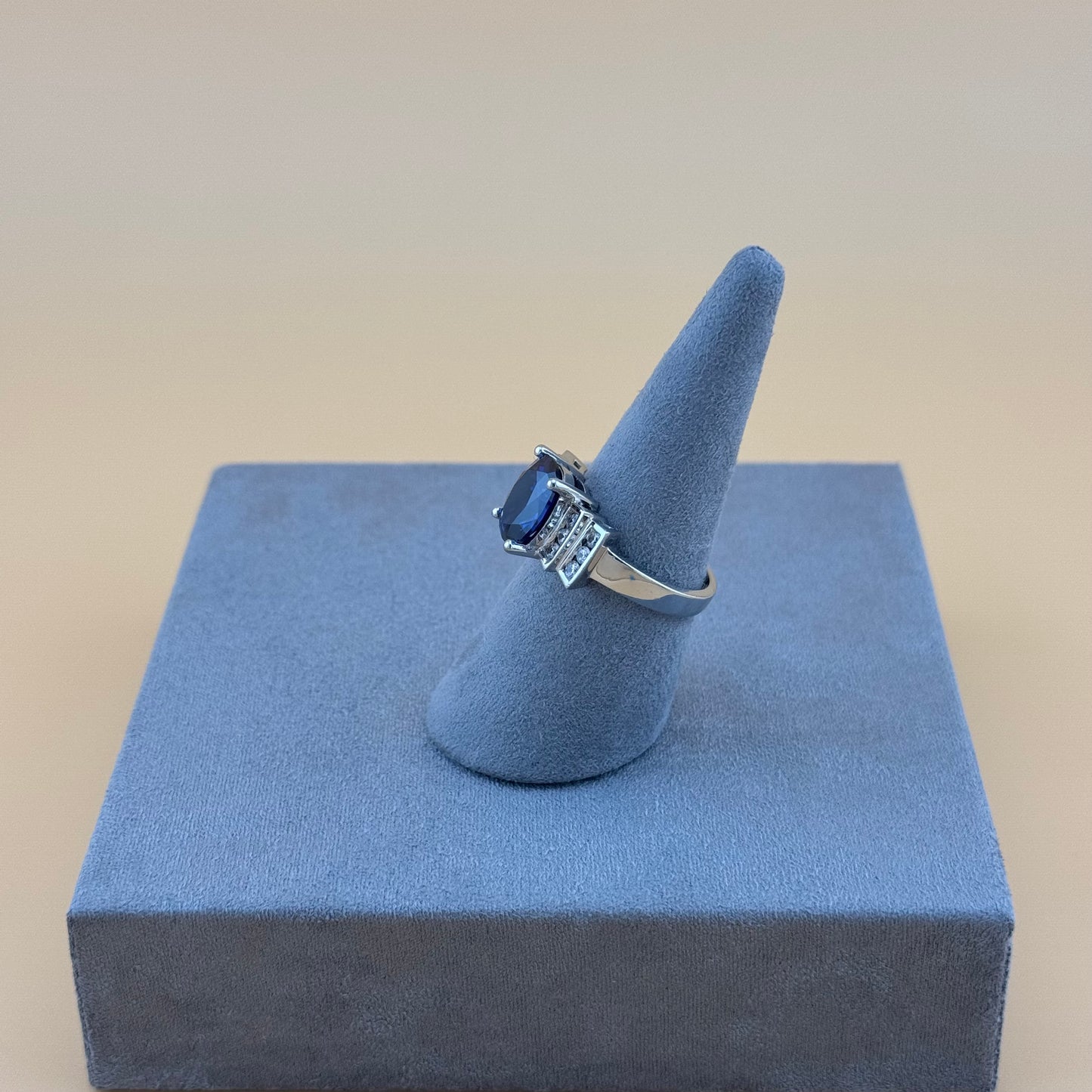 Silver ring with a blue sapphire gemstone on a blue stand against a beige background