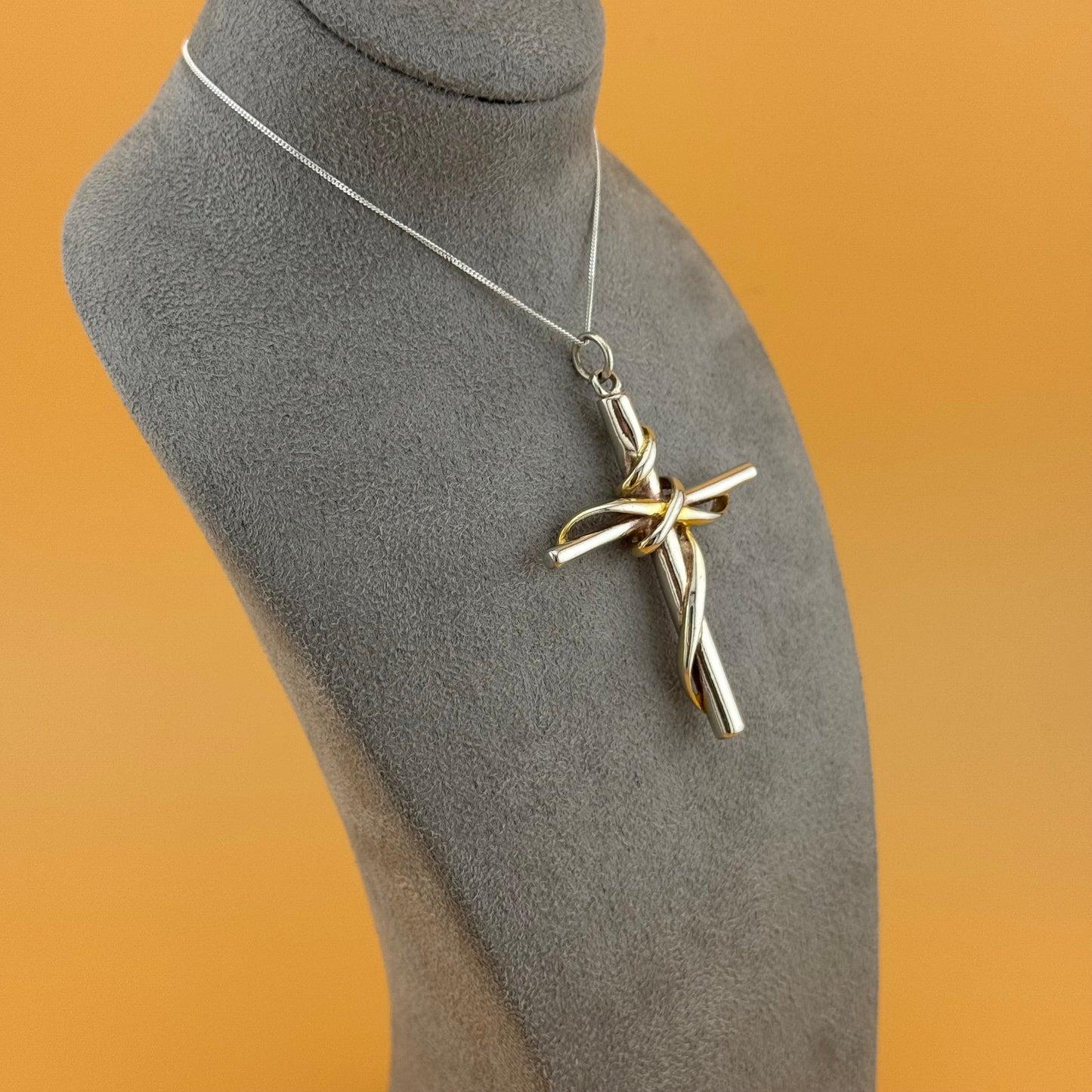 Silver cross pendant on a mannequin bust with a brown background
