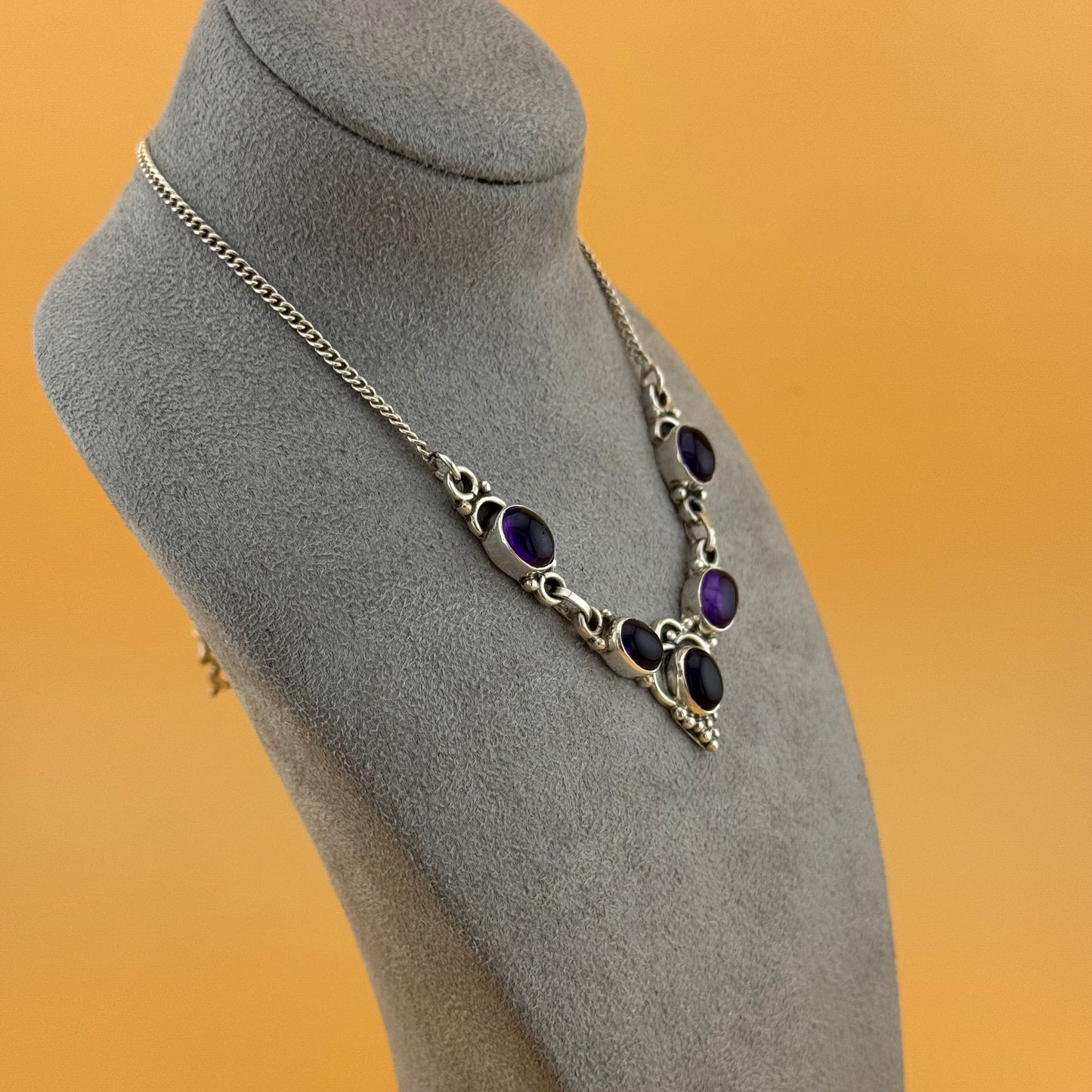 Necklace with purple stones on a gray mannequin bust against an orange background