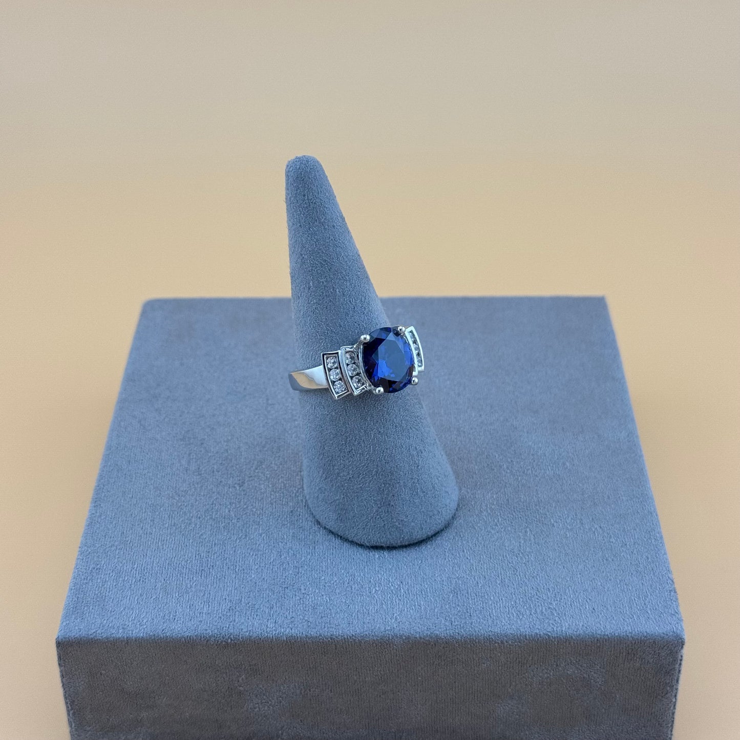 Ring with a blue sapphire gemstone on a gray stand against a beige background