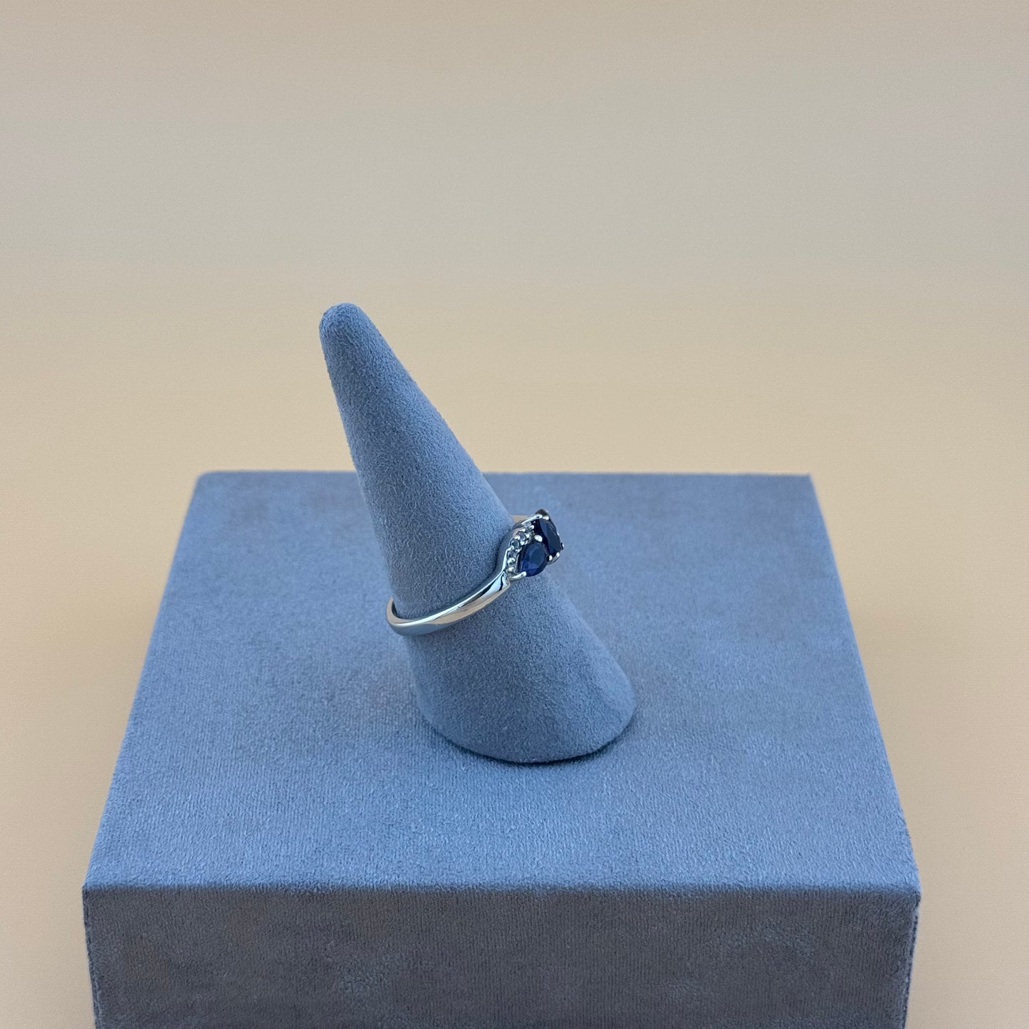 Silver ring with a blue tanzanite gemstone on a blue cone-shaped stand against a beige background