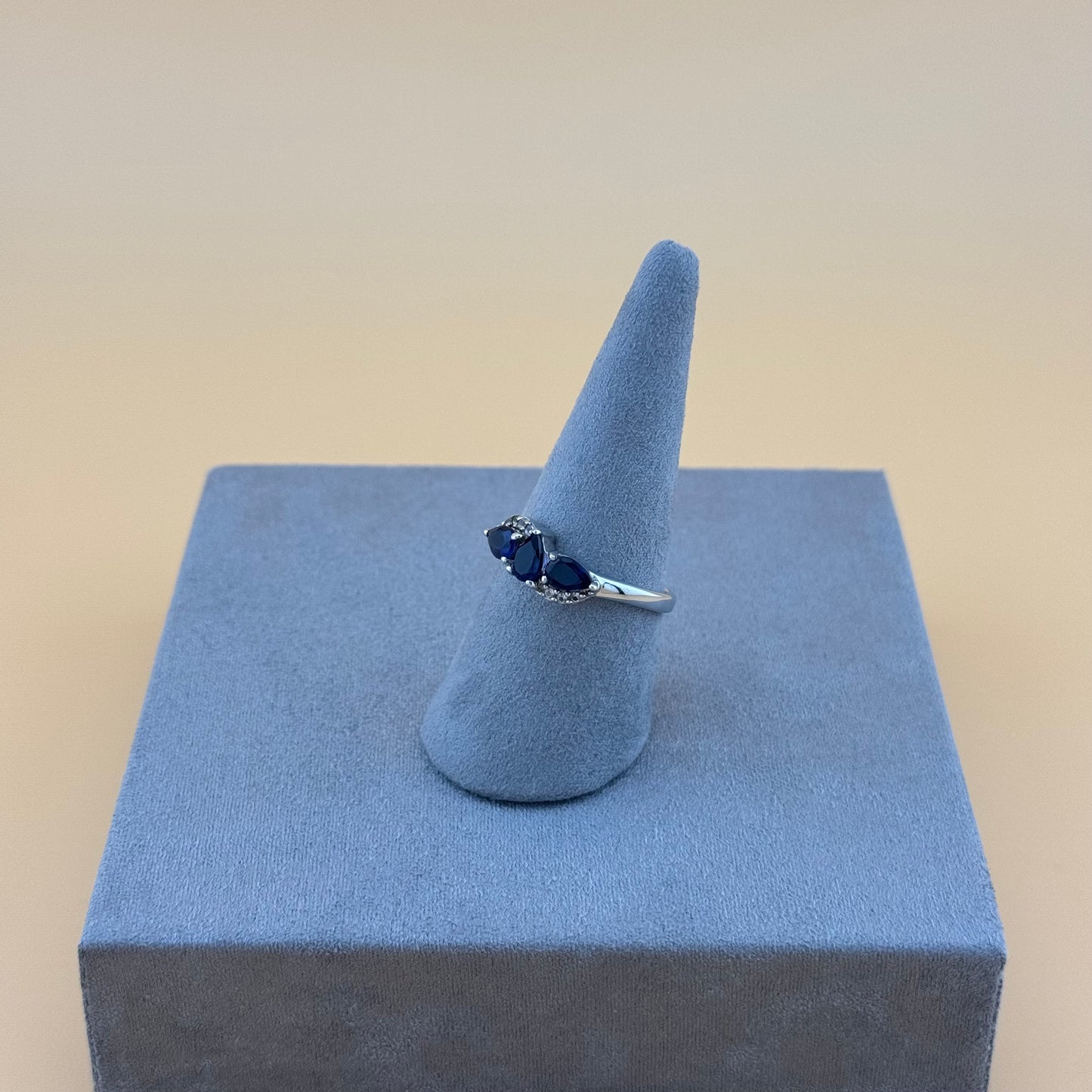 Silver ring with blue tanzanite stones on a blue stand against a beige background