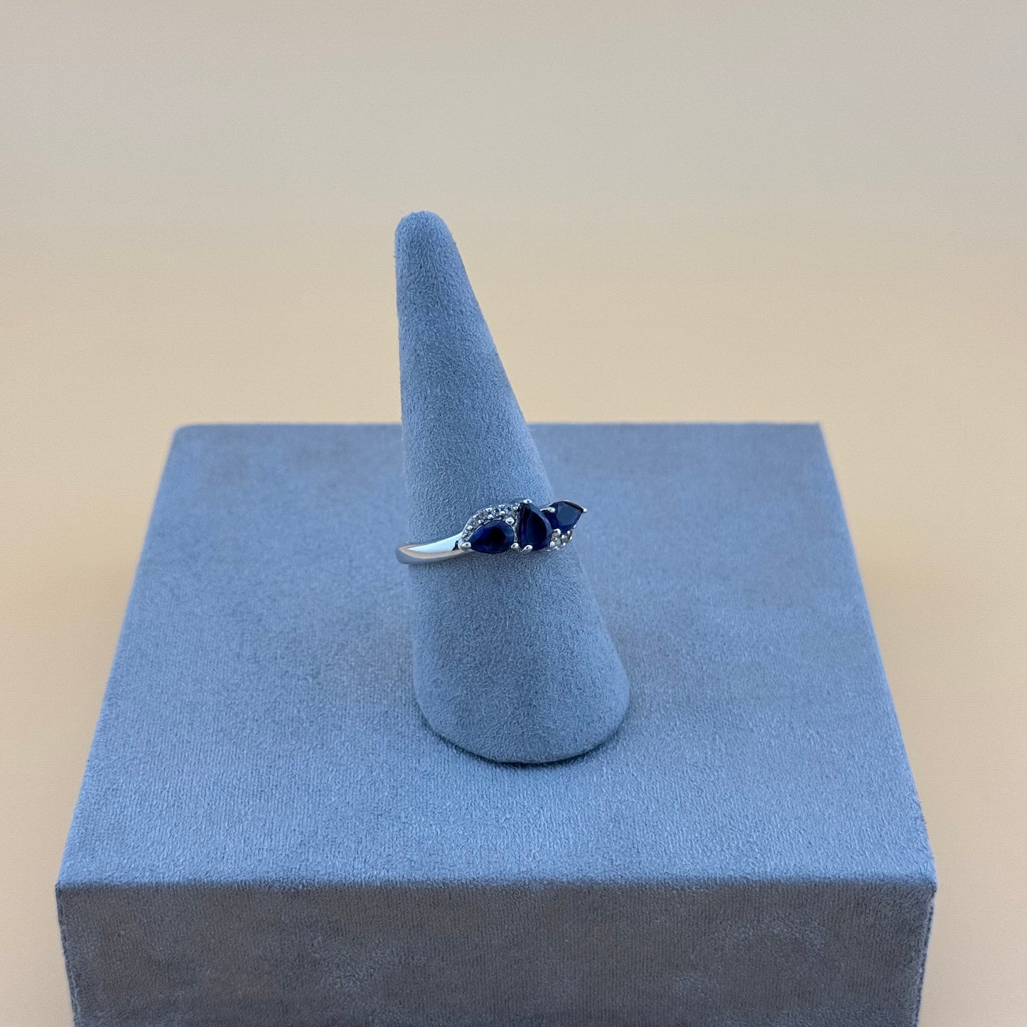 Silver ring with blue tanzanite stones on a blue stand against a beige background