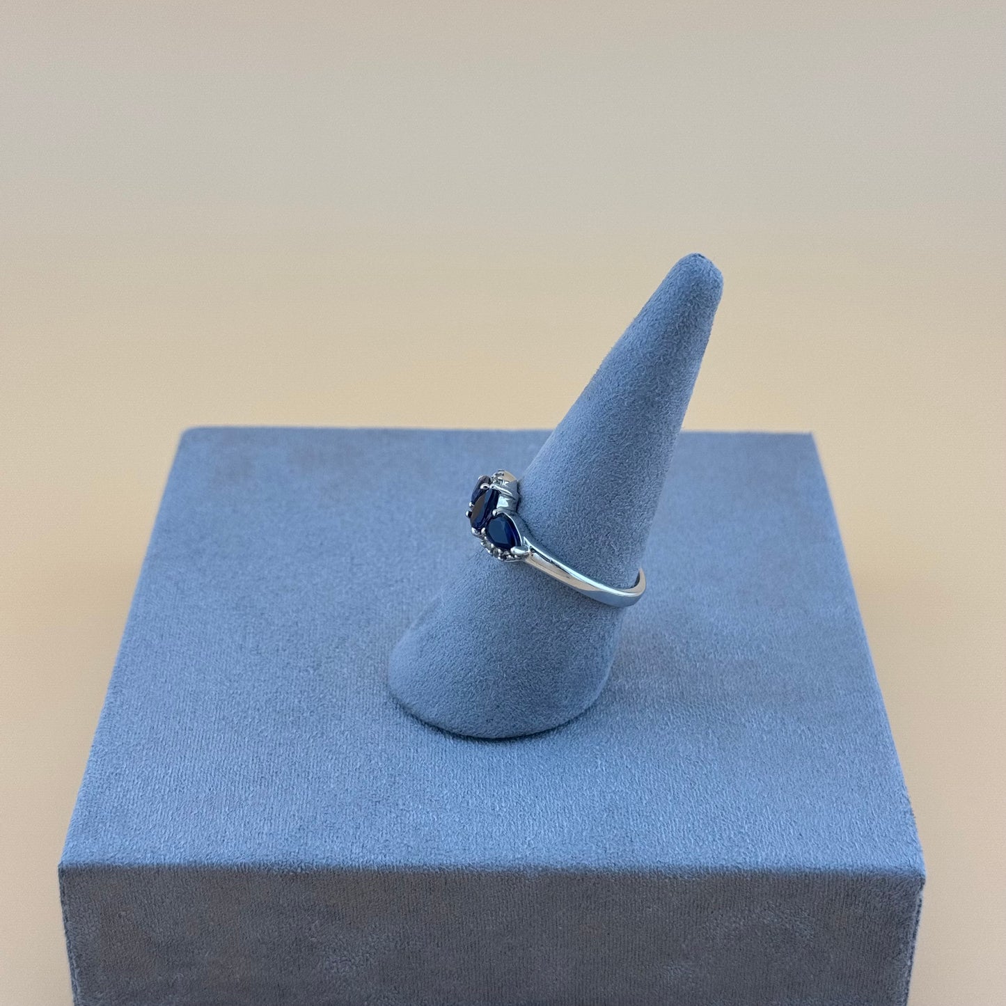 Silver ring with a blue tanzanite gemstone on a blue cone-shaped stand against a beige background