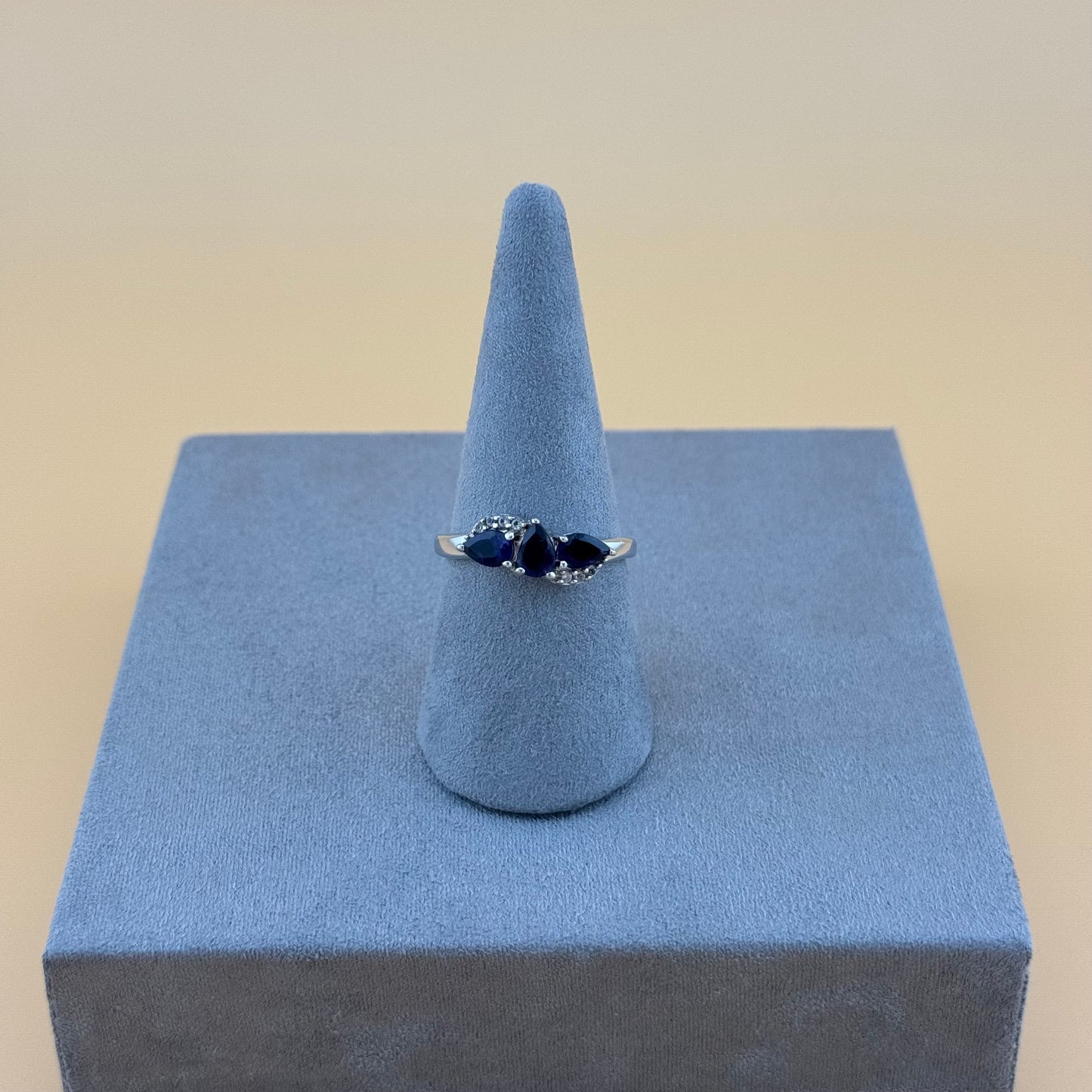 Silver tanzanite ring with a blue gemstone on a blue stand against a beige background