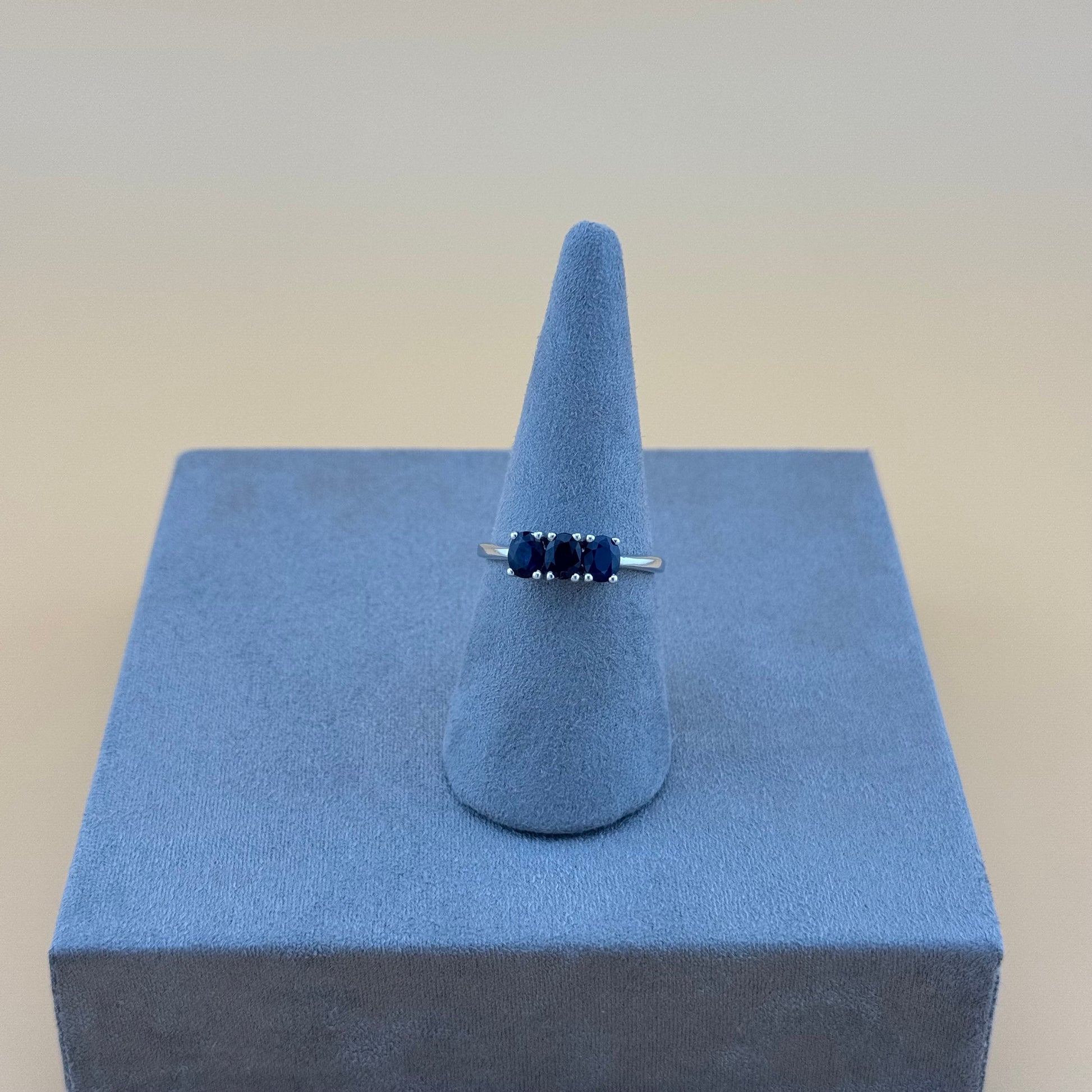 Ring with blue sapphire stones on a blue stand against a beige background