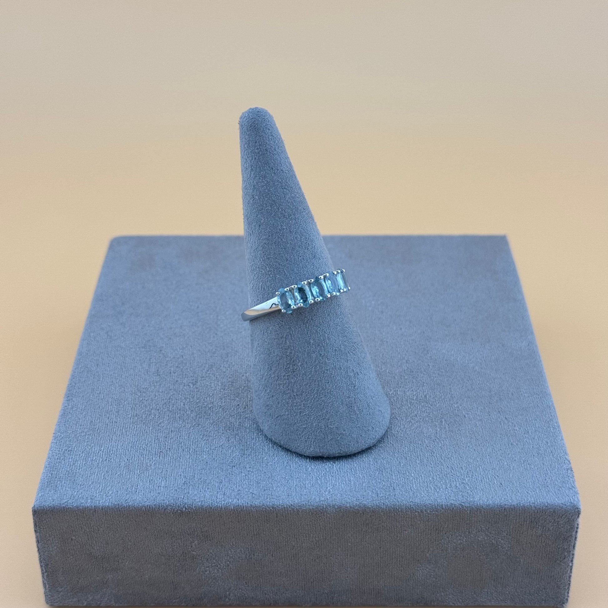 Aquamarine 5 stone Ring on a blue stand with a beige background