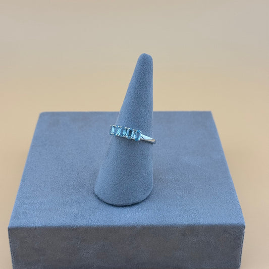 Silver ring with blue Aquamarine gemstones on a gray cone-shaped stand against a beige background
