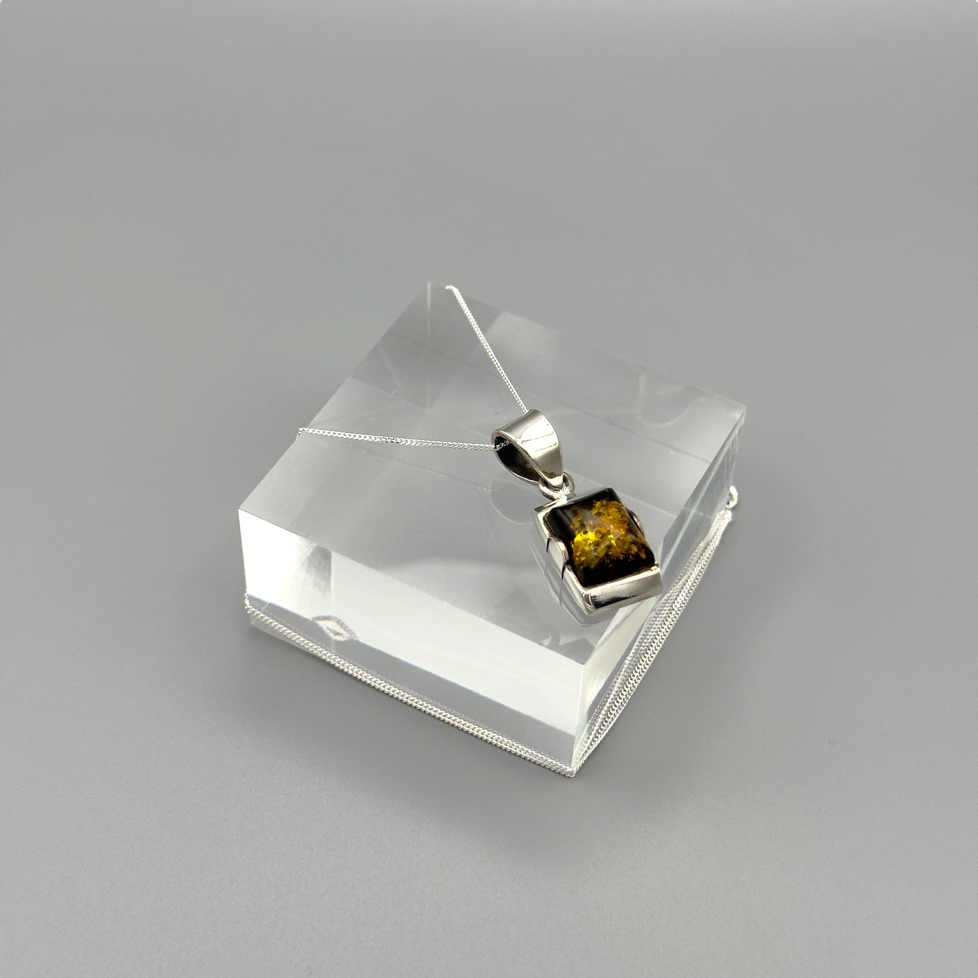 Silver pendant with Baltic Amber on a clear stand against a grey background
