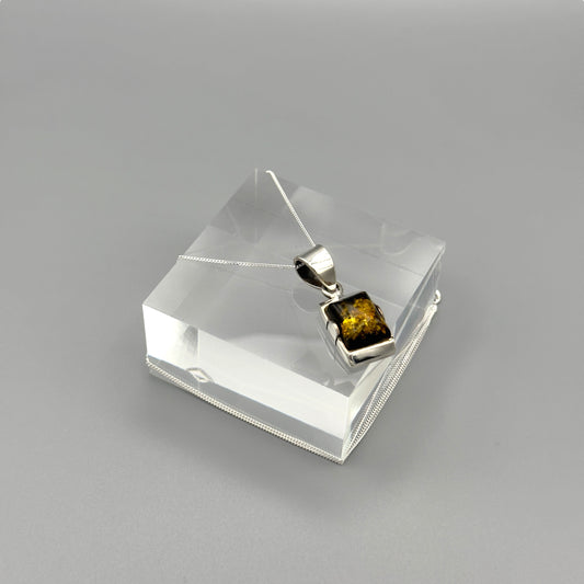 Silver pendant with Baltic Amber on a clear stand against a grey background