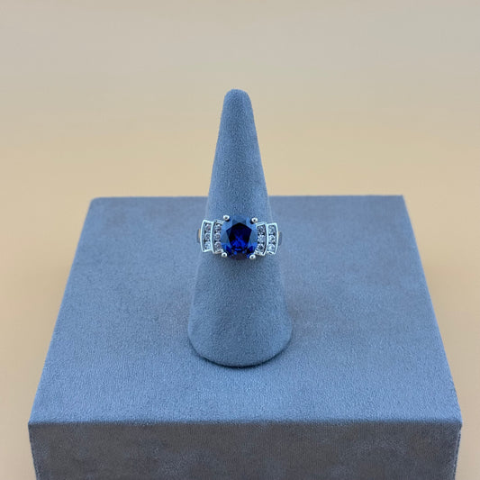 Ring with a blue sapphire gemstone on a gray stand against a beige background
