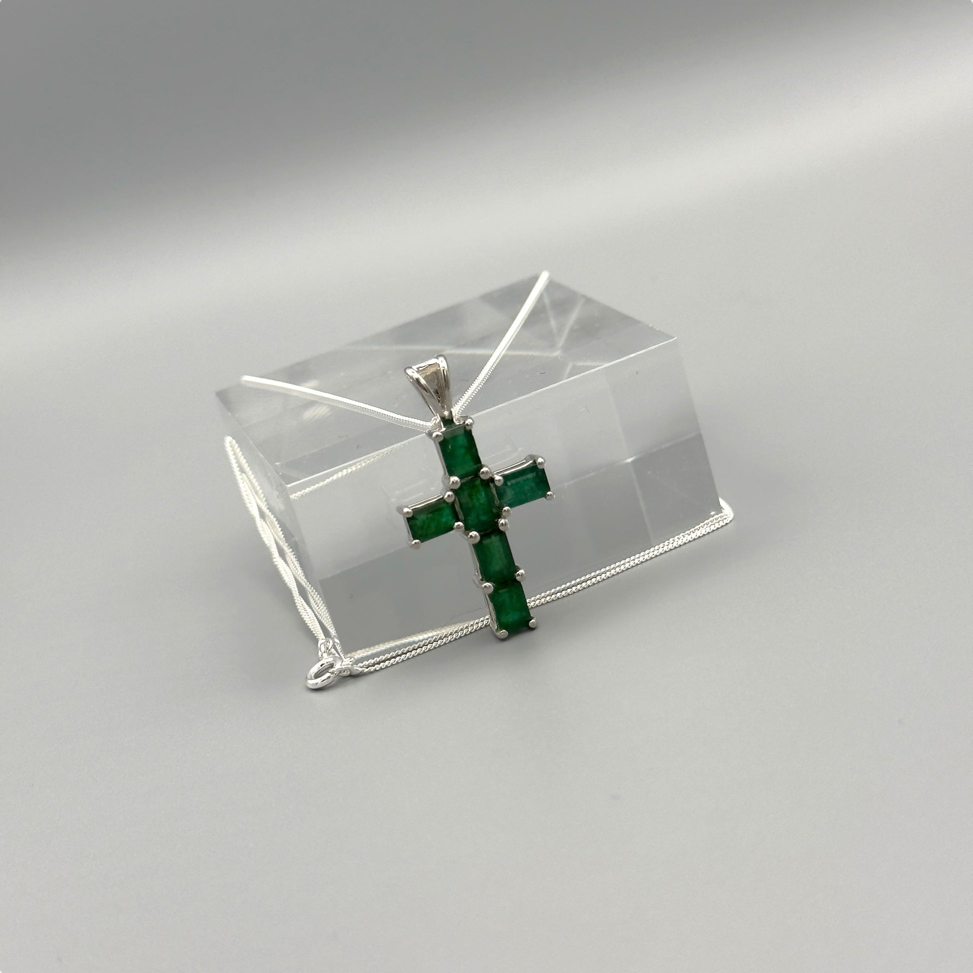 Emerald cross pendant on silver box chain displayed on clear block