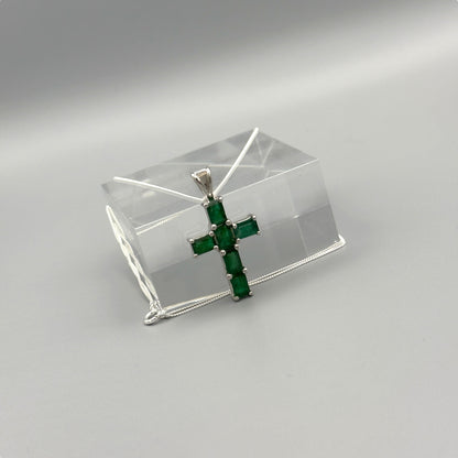 Emerald cross pendant on silver box chain displayed on clear block