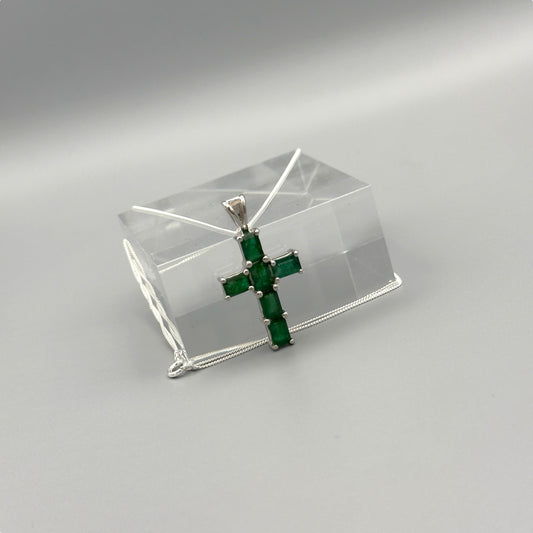 Emerald cross pendant on silver box chain displayed on clear block