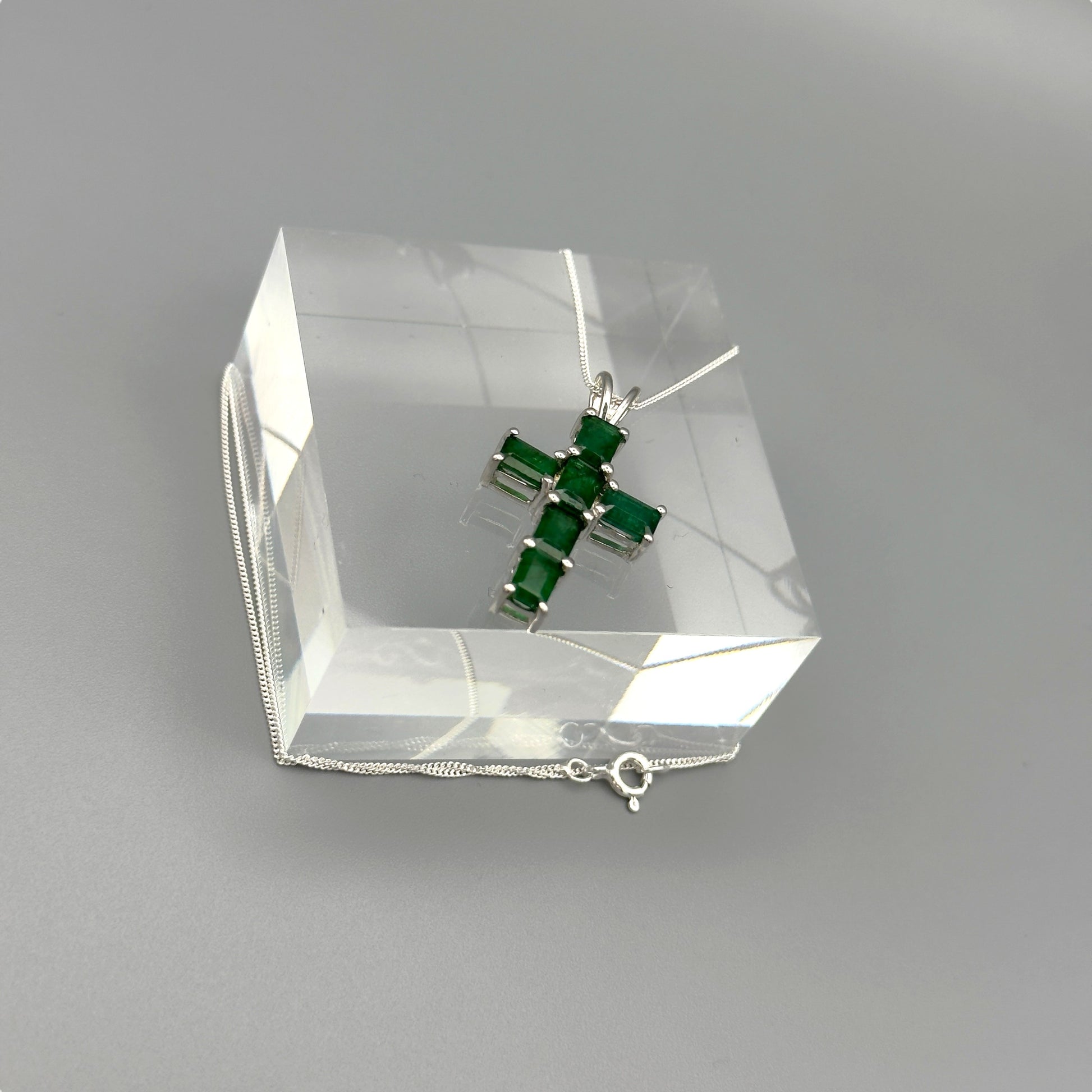 Angled emerald cross necklace on display block with reflections