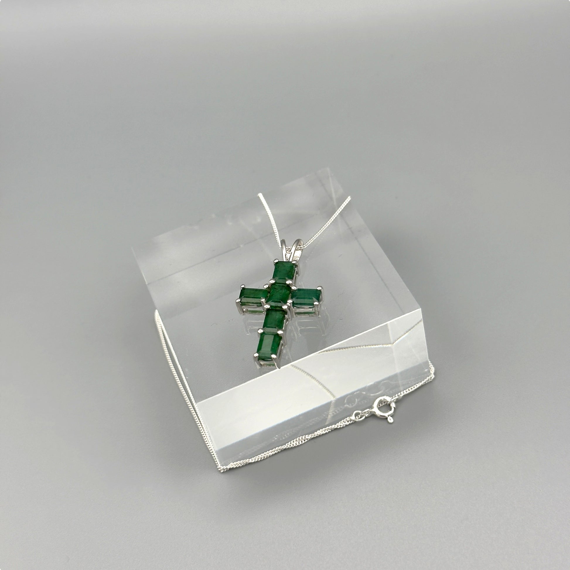 Full view of silver cross necklace laid over crystal block