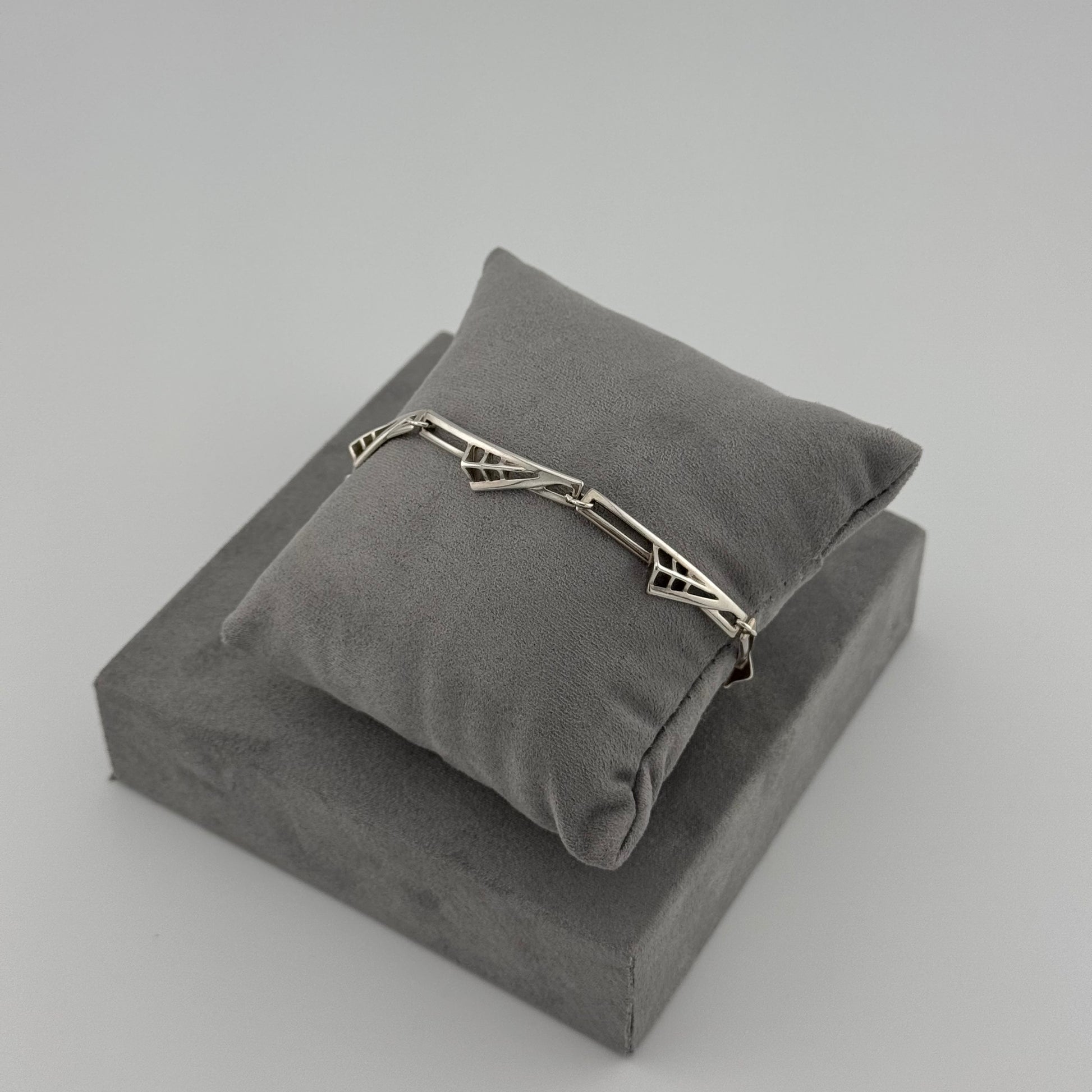 silver bracelet with a geometric pattern n a grey cushion 