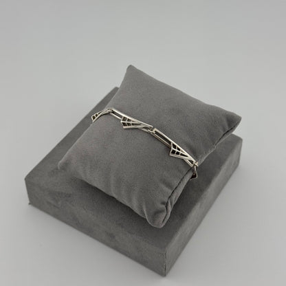 silver bracelet with a geometric pattern n a grey cushion 