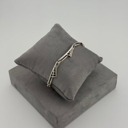 silver bracelet with a geometric pattern n a grey cushion 