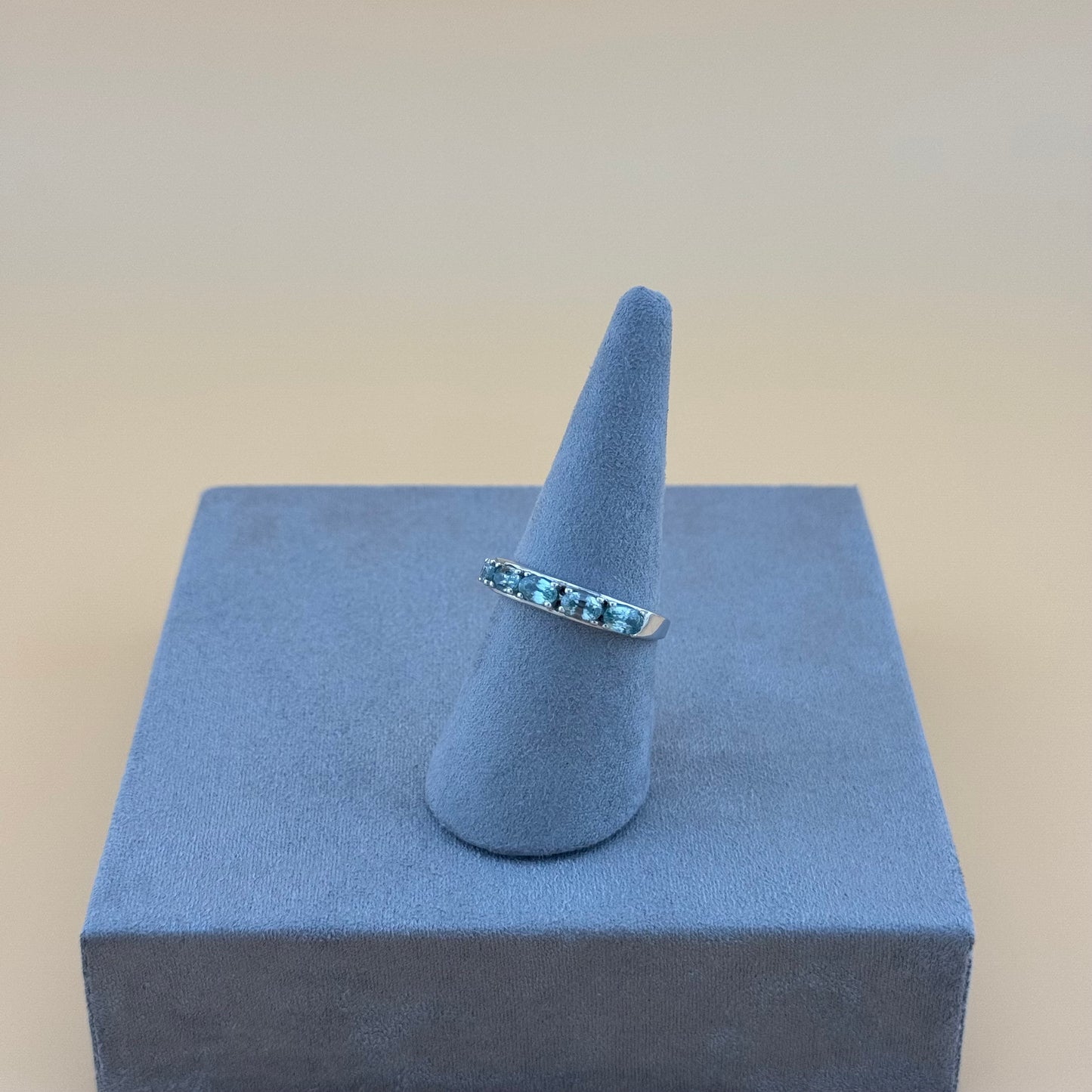 Silver ring with blue gemstones on a blue cone and square block against a beige background