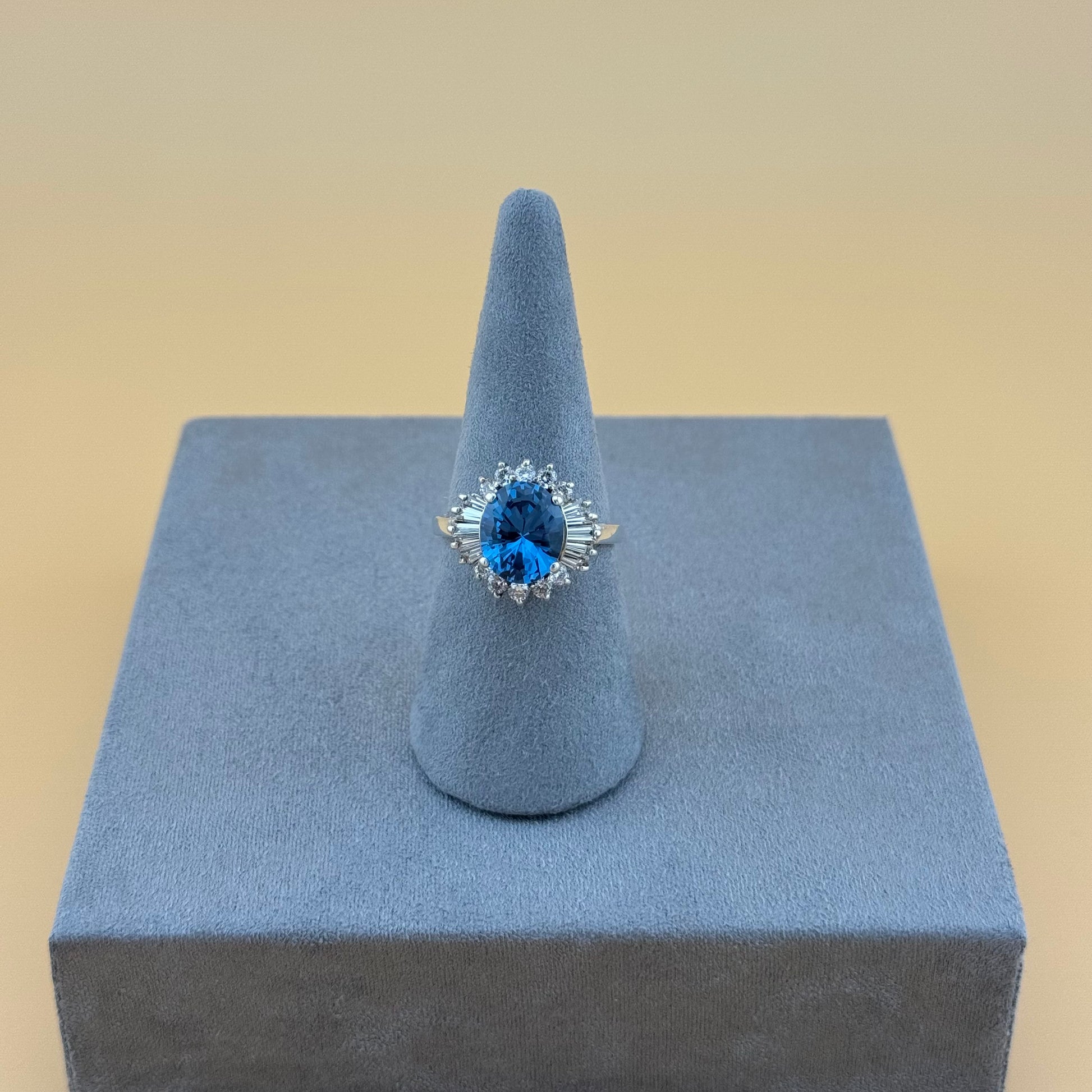 Ring with blue topaz gemstone on a gray stand against a beige background
