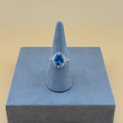 Ring with blue topaz gemstone on a gray stand against a beige background