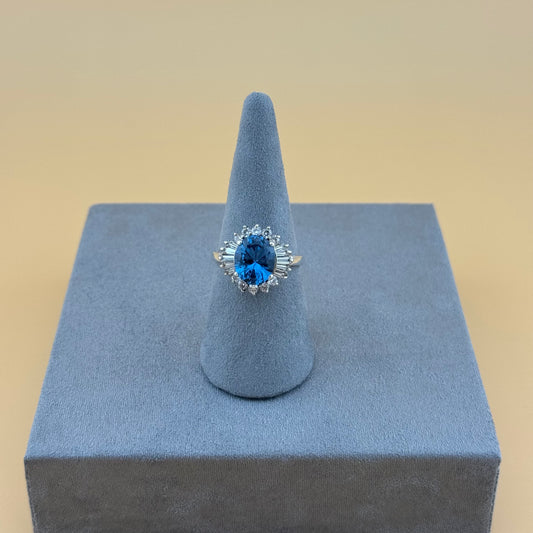 Ring with blue topaz gemstone on a gray stand against a beige background