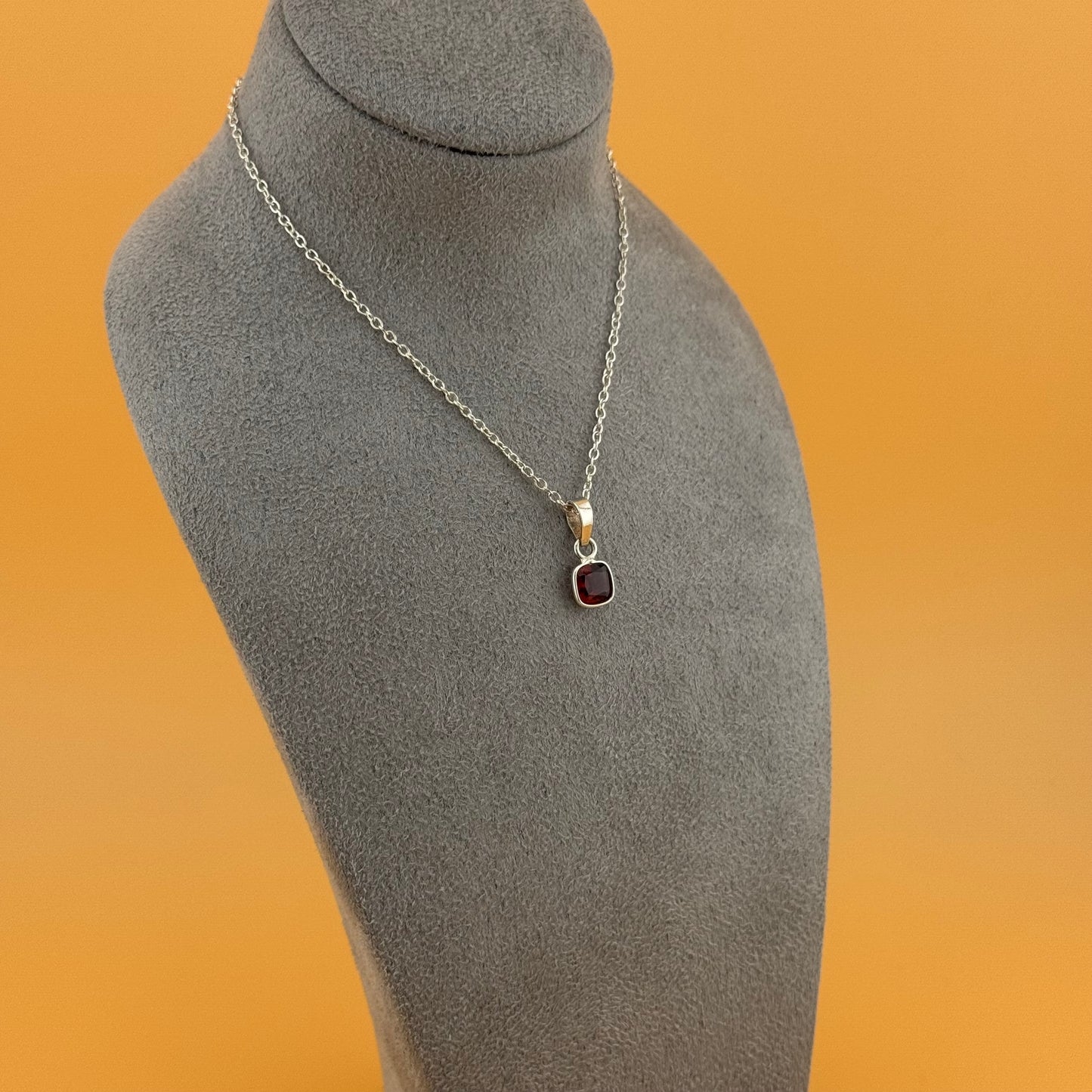 Necklace with a garnet pendant on a gray mannequin bust against an orange background