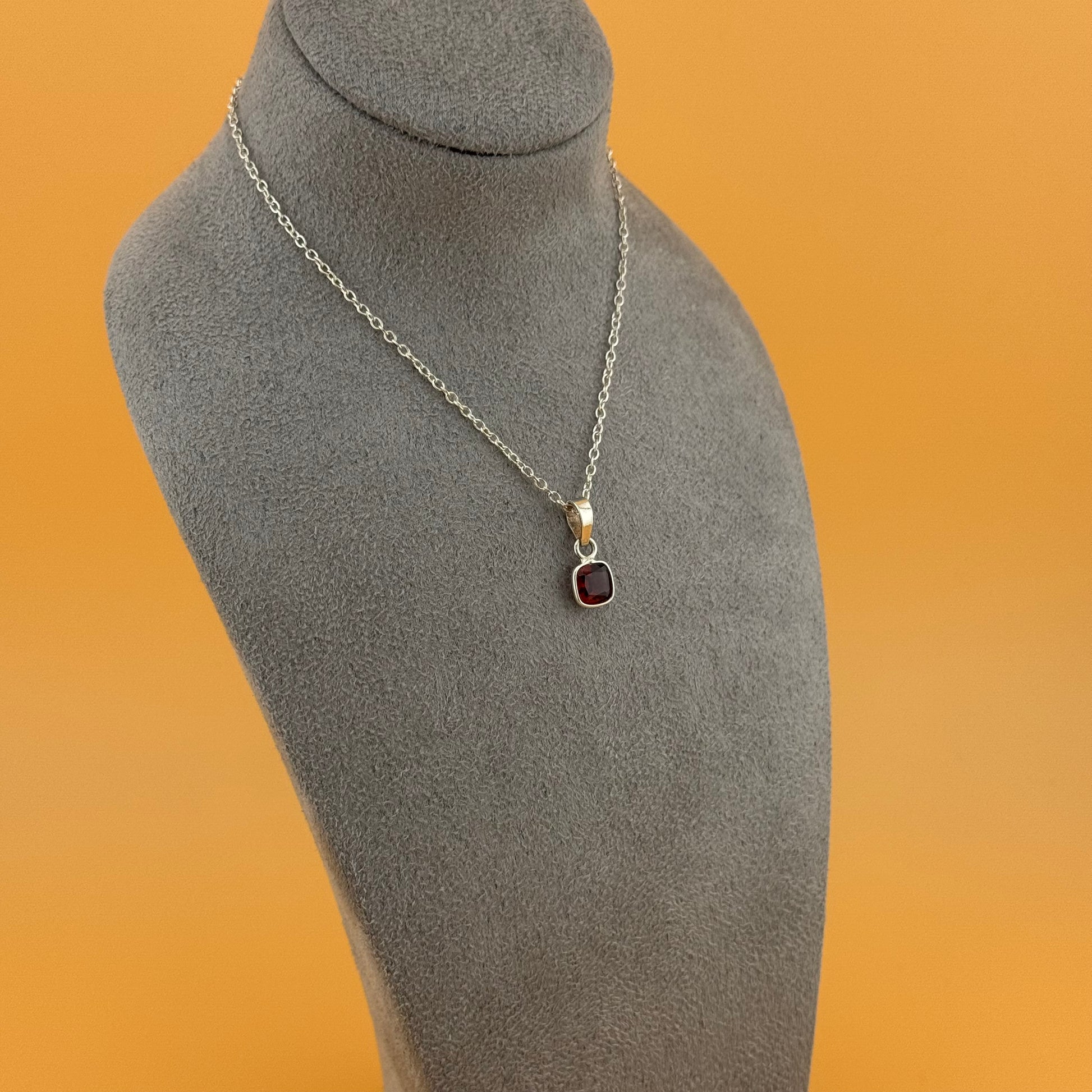 Necklace with a garnet pendant on a gray mannequin bust against an orange background