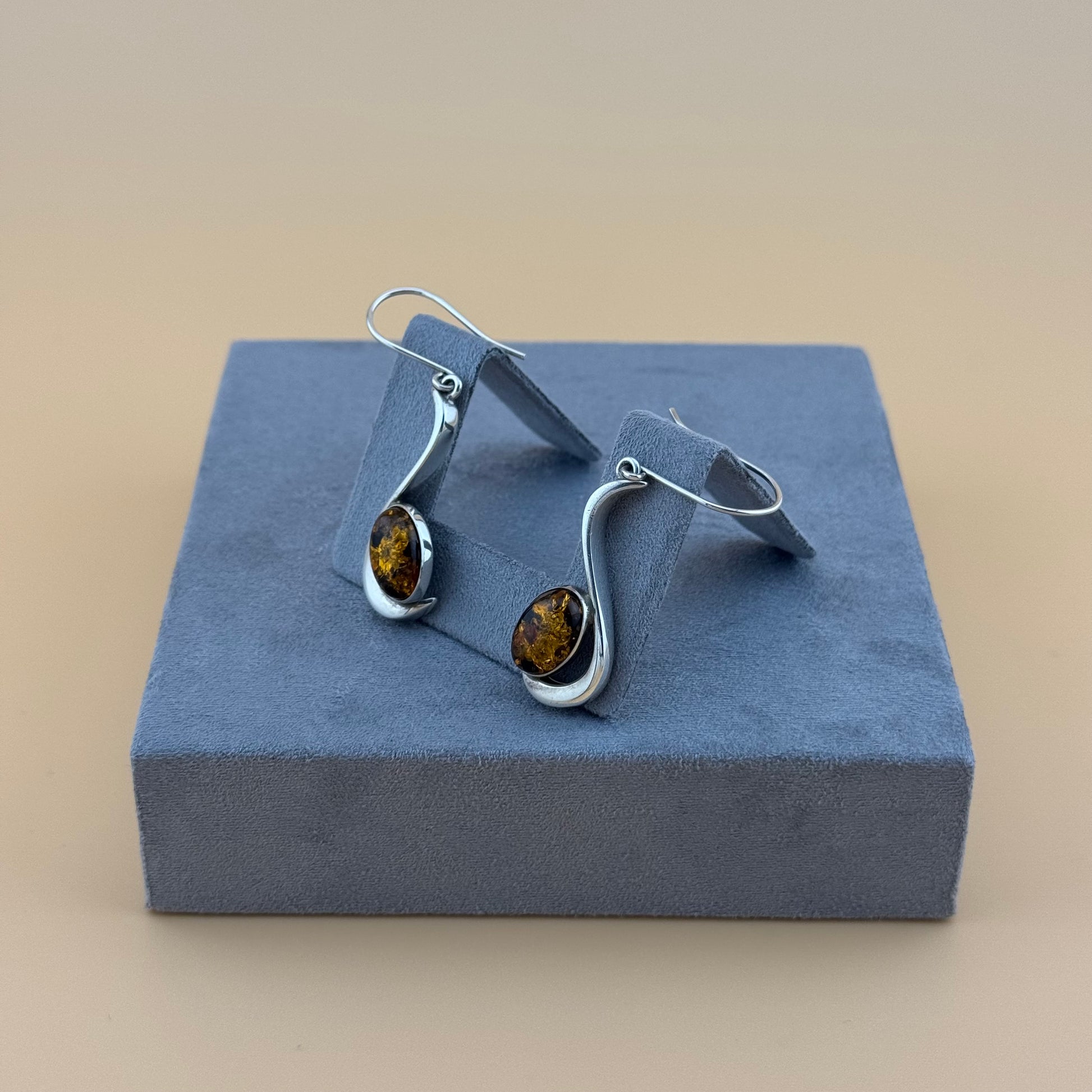 Silver earrings with amber stones on a blue jewelry display box.