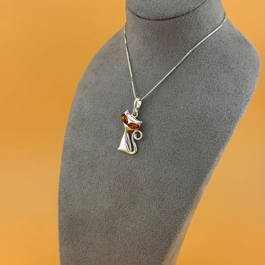 Silver cat-shaped pendant with amber gemstone on a mannequin bust against an orange background