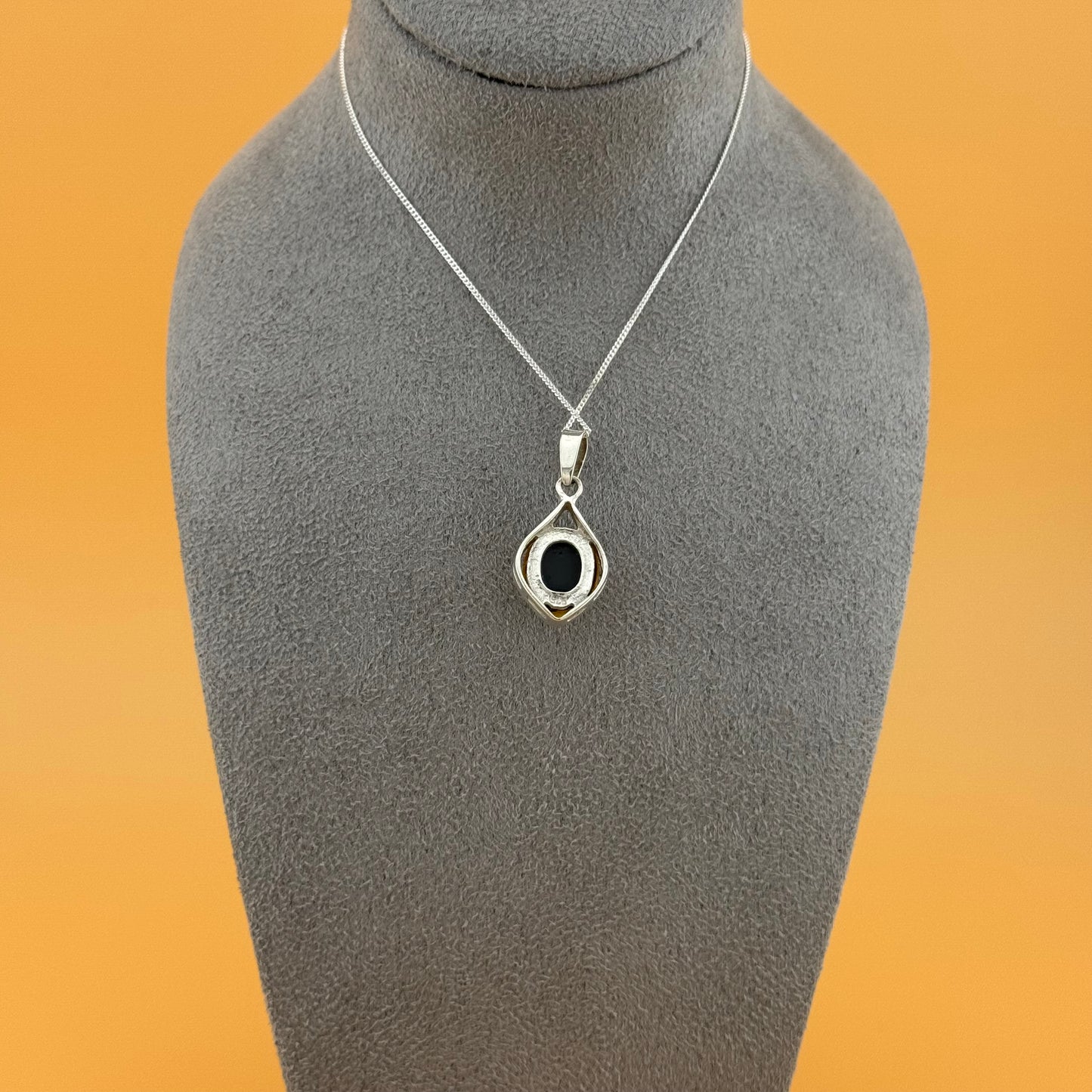 Silver necklace with a pendant on a gray mannequin bust against an orange background