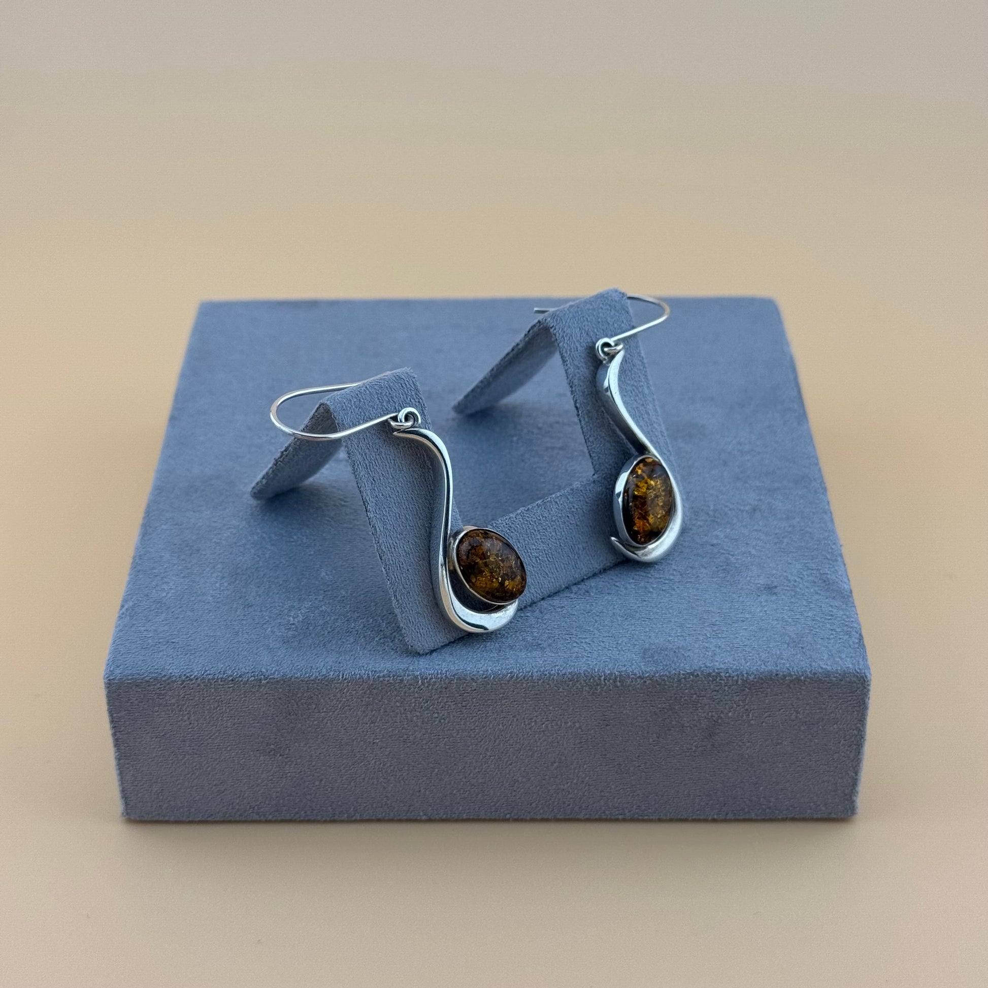 Pair of silver earrings with amber stones on a blue cushioned stand.