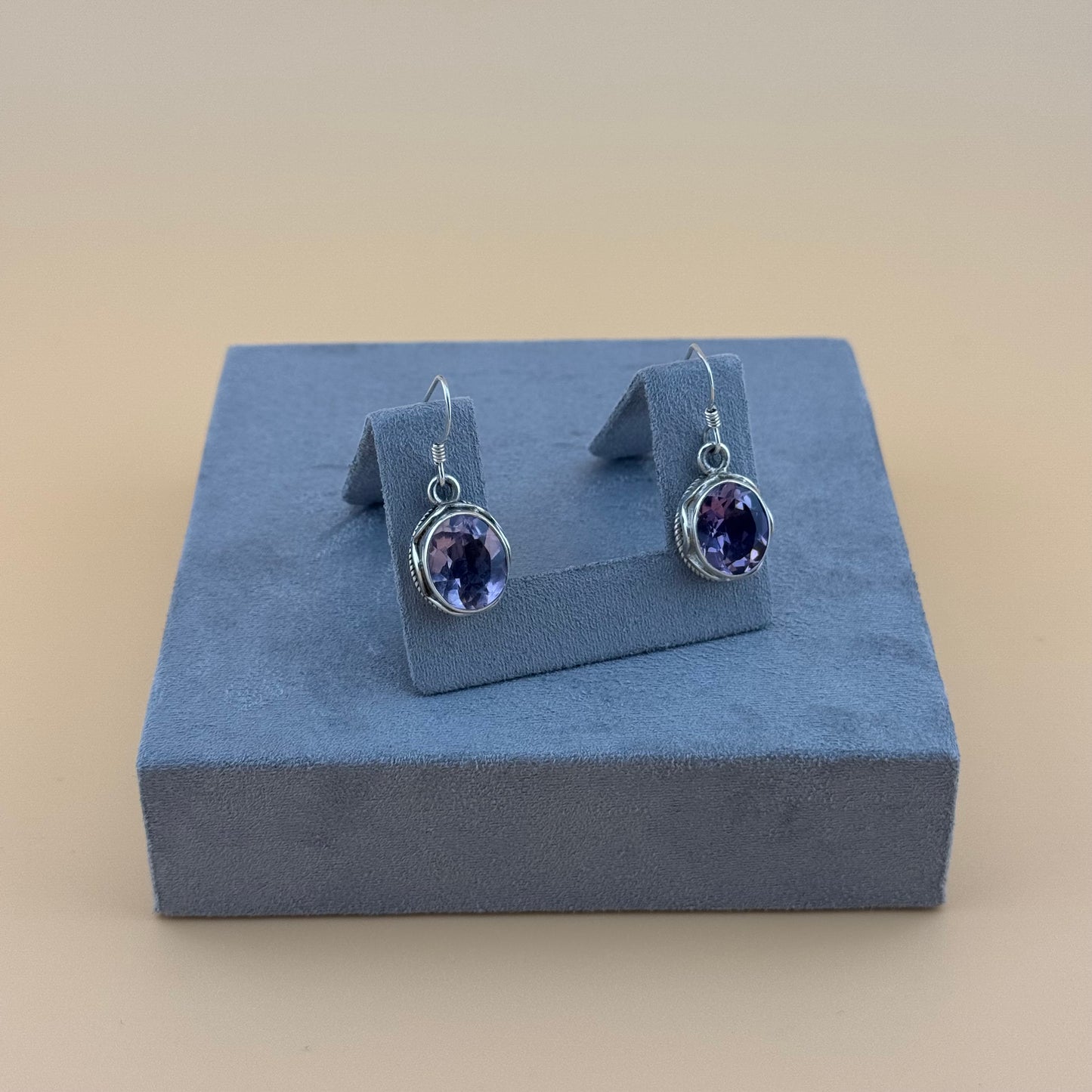 Pair of purple amethyst gemstone earrings on a blue jewellery display box against a beige background