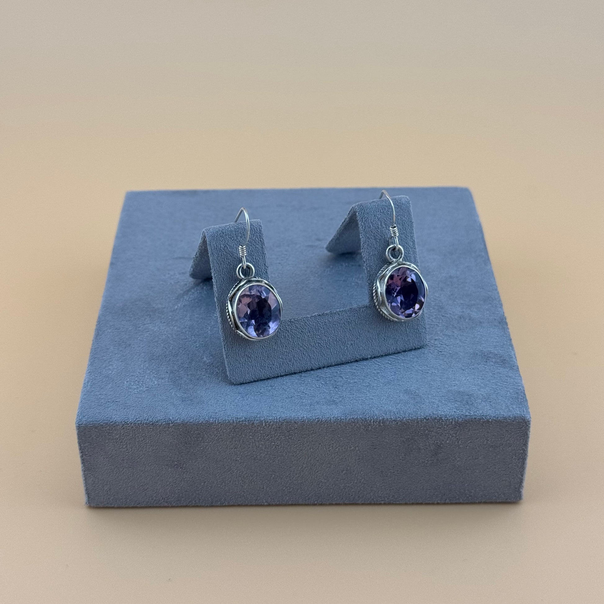 Pair of purple amethyst gemstone earrings on a blue jewellery display box against a beige background